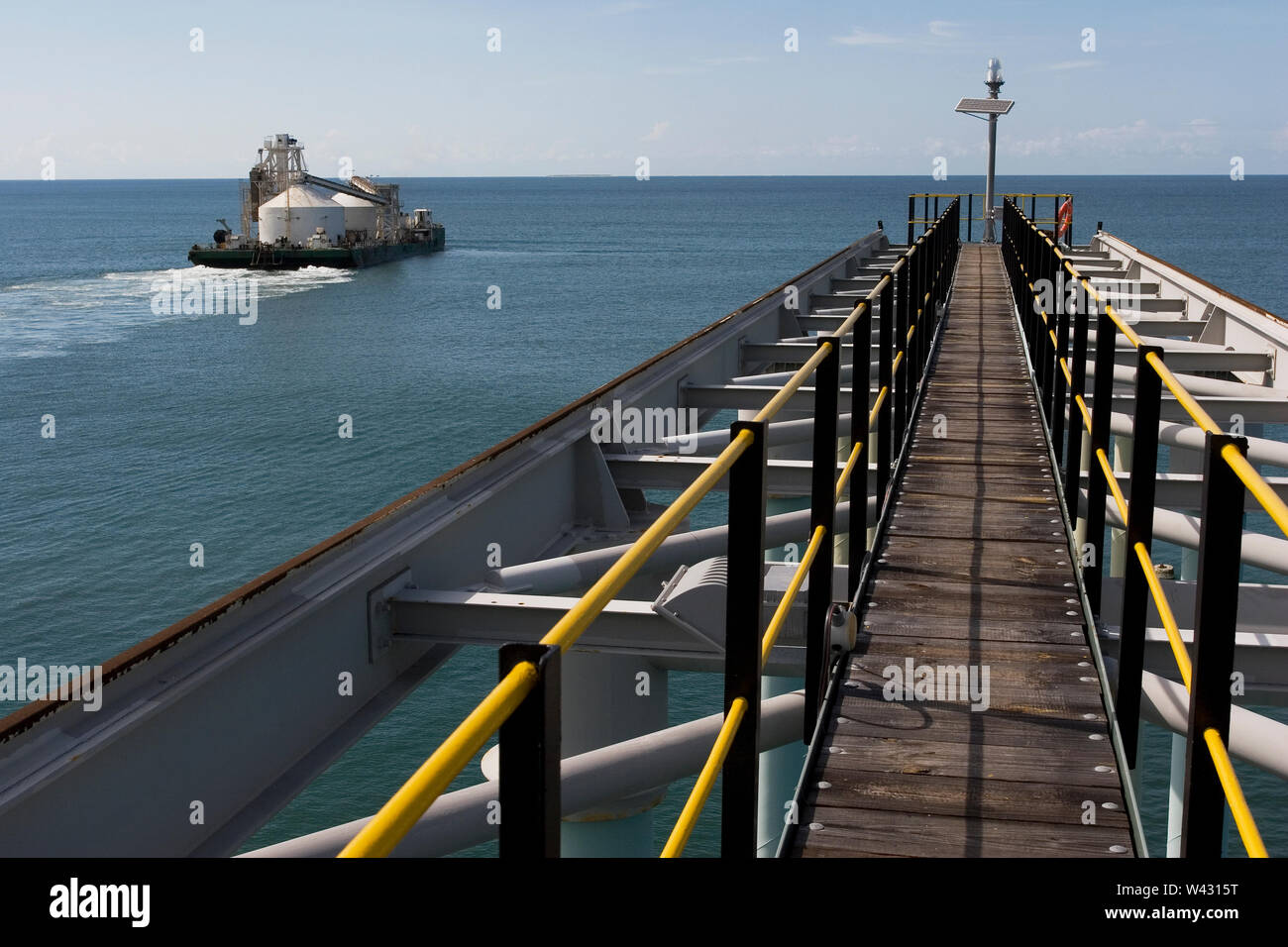 Mining, managing & transporting of titanium mineral sands. Barge leaving port to discharge product into OGV at sea & showing jetty infrastructure . Stock Photo
