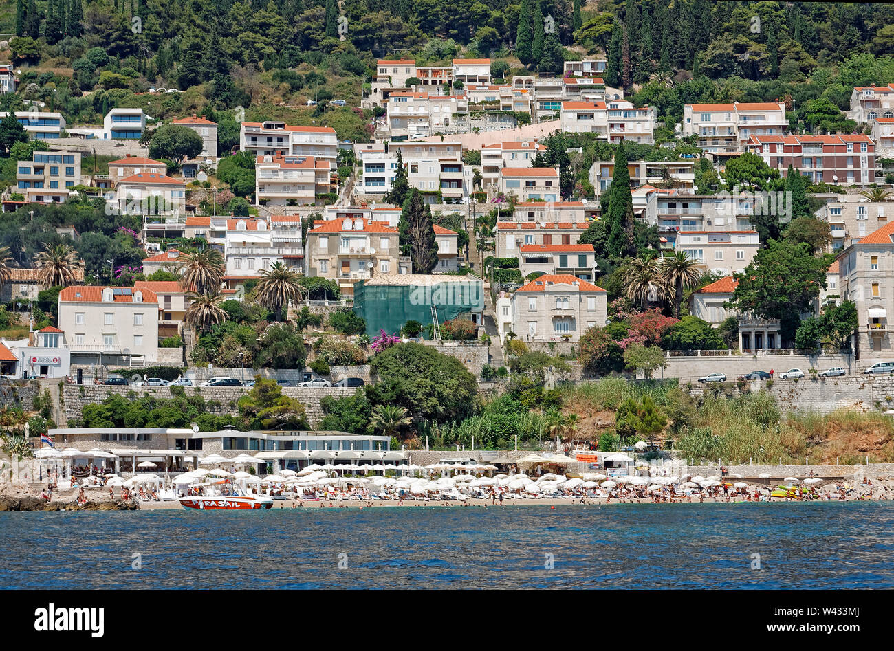 coastline, city scene, crowded beach, umbrellas, people, buildings up hillside, water, Adriatic