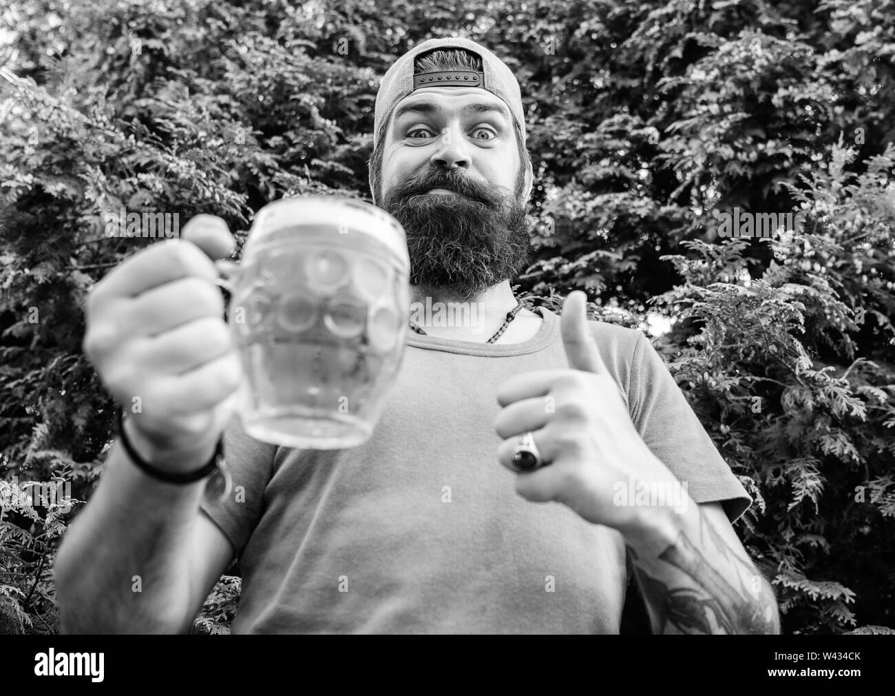 Thumbs up to the best beer. Man drinker holding beer mug. Bearded man enjoy drinking beer on nature. Brutal hipster with long beard having craft beer. Stock Photo