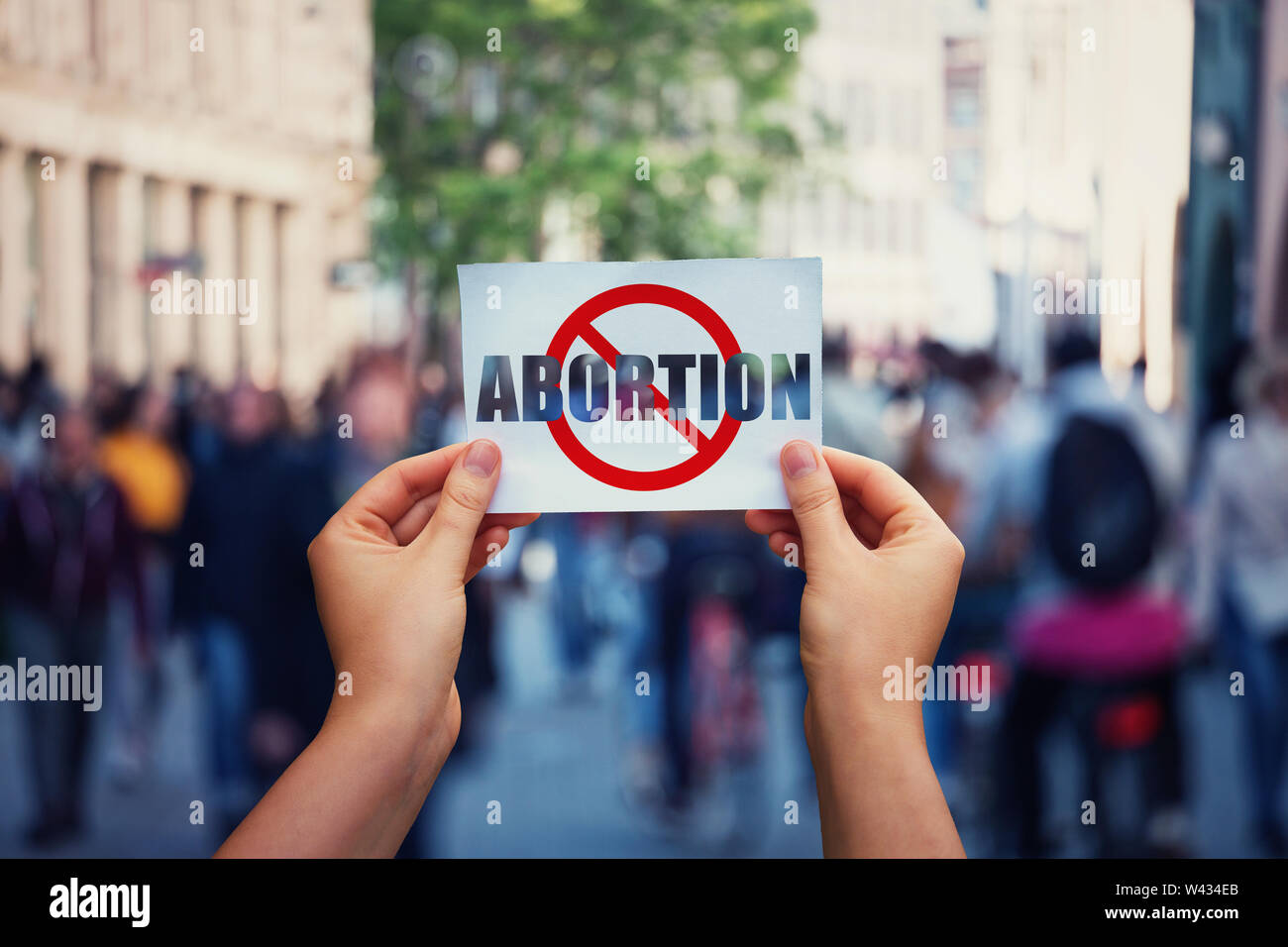 Activist hands holding a banner with stop abortion message over a crowded street background. Social awareness concept, humanity problems say no to abo Stock Photo