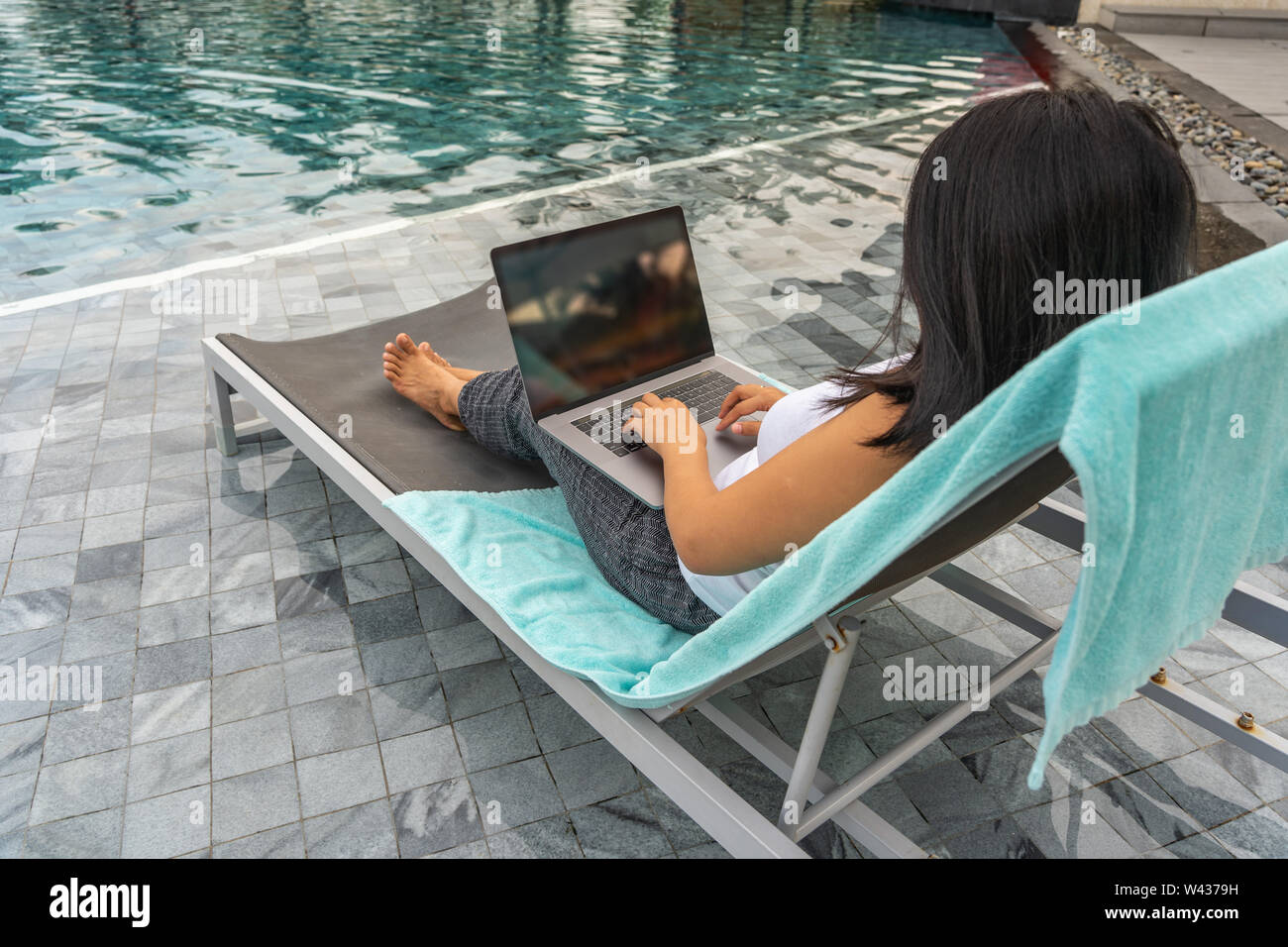Woman Using Laptop While Sitting On Bench At Swimming Pool Stock