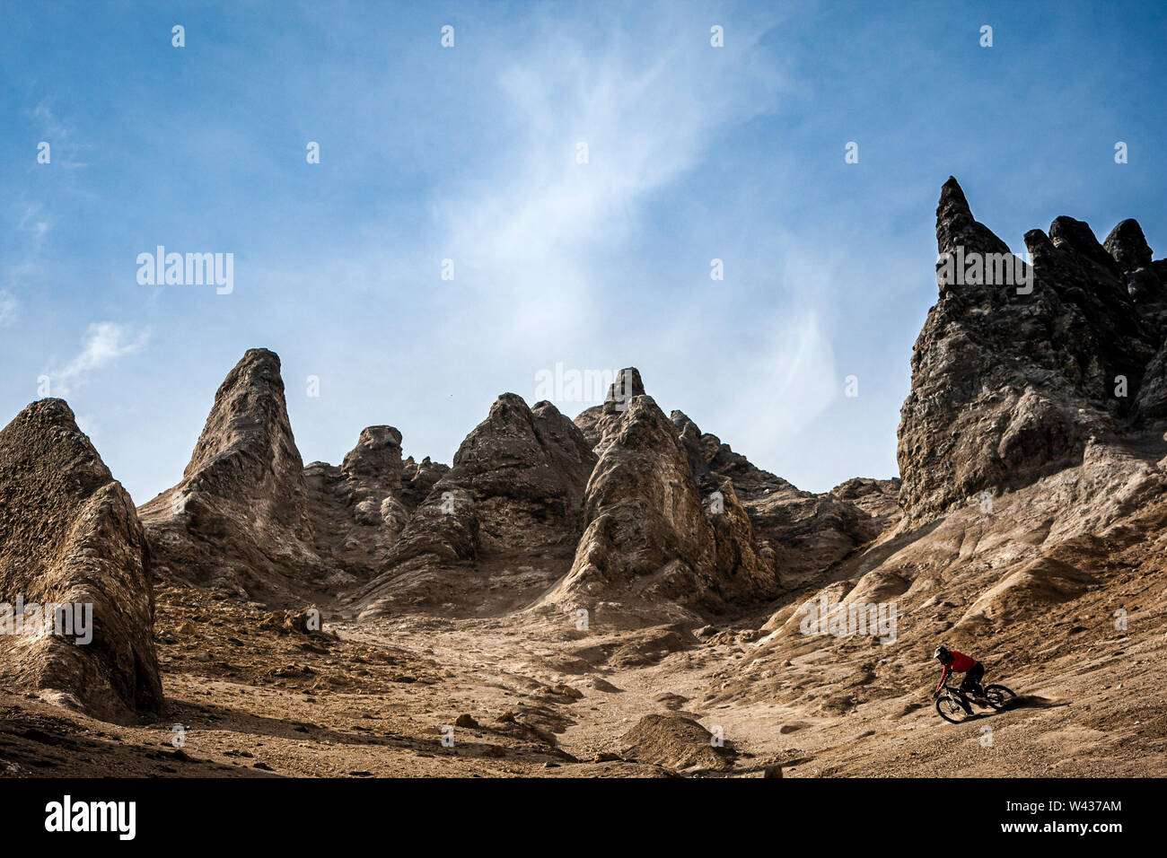 A mountain biker riding down a steep sandy hillside with strange rock formations behind Stock Photo
