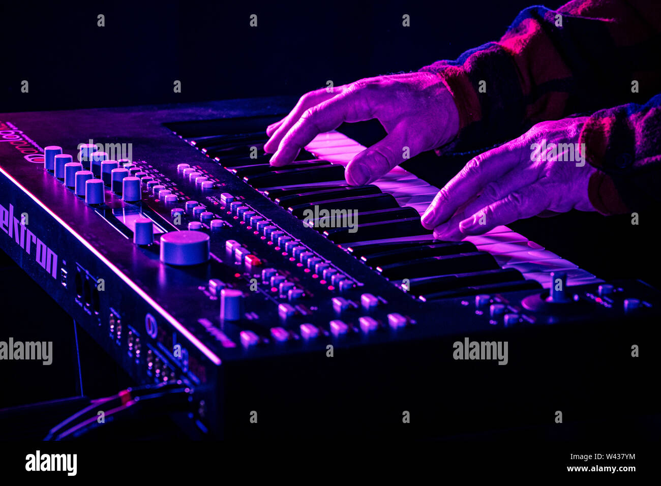 Closeup of male hands playing a modern synthesizer keyboard under stage lighting. Stock Photo