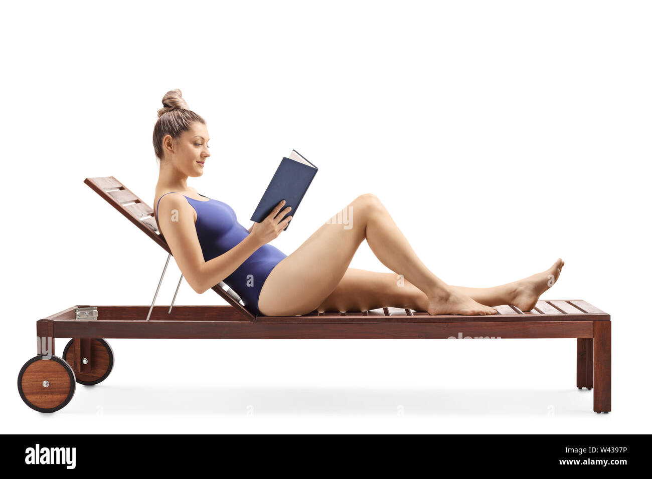 Full length shot of a young woman reading a book and relaxing on a sunbed isolated on white background Stock Photo