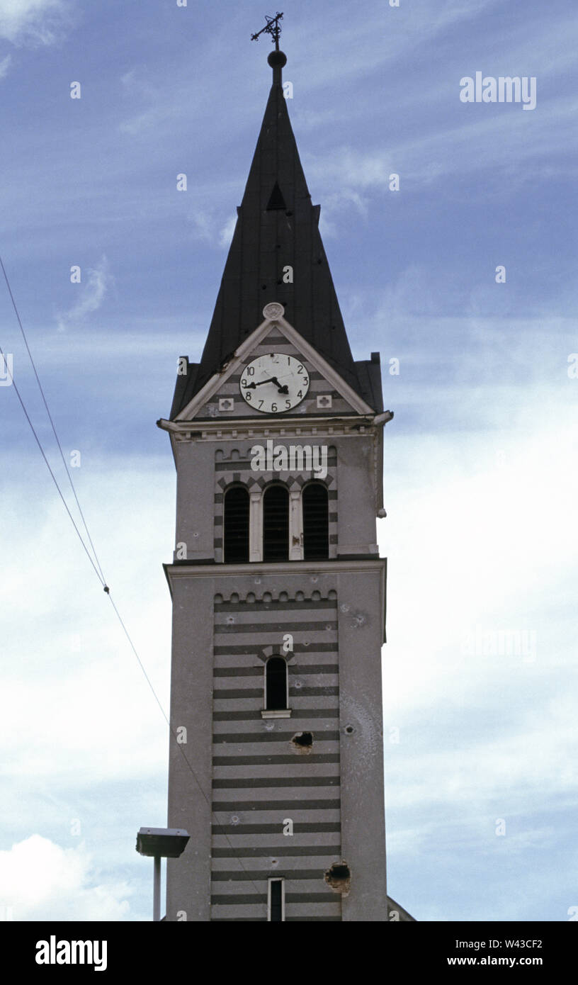 12th April 1993 During the Siege of Sarajevo: bullet and shell holes in the clock tower of the Church of the Holy Trinity on Sniper Alley (Zmaja od Bosne), in the Dolac Malta area of the city. Stock Photo