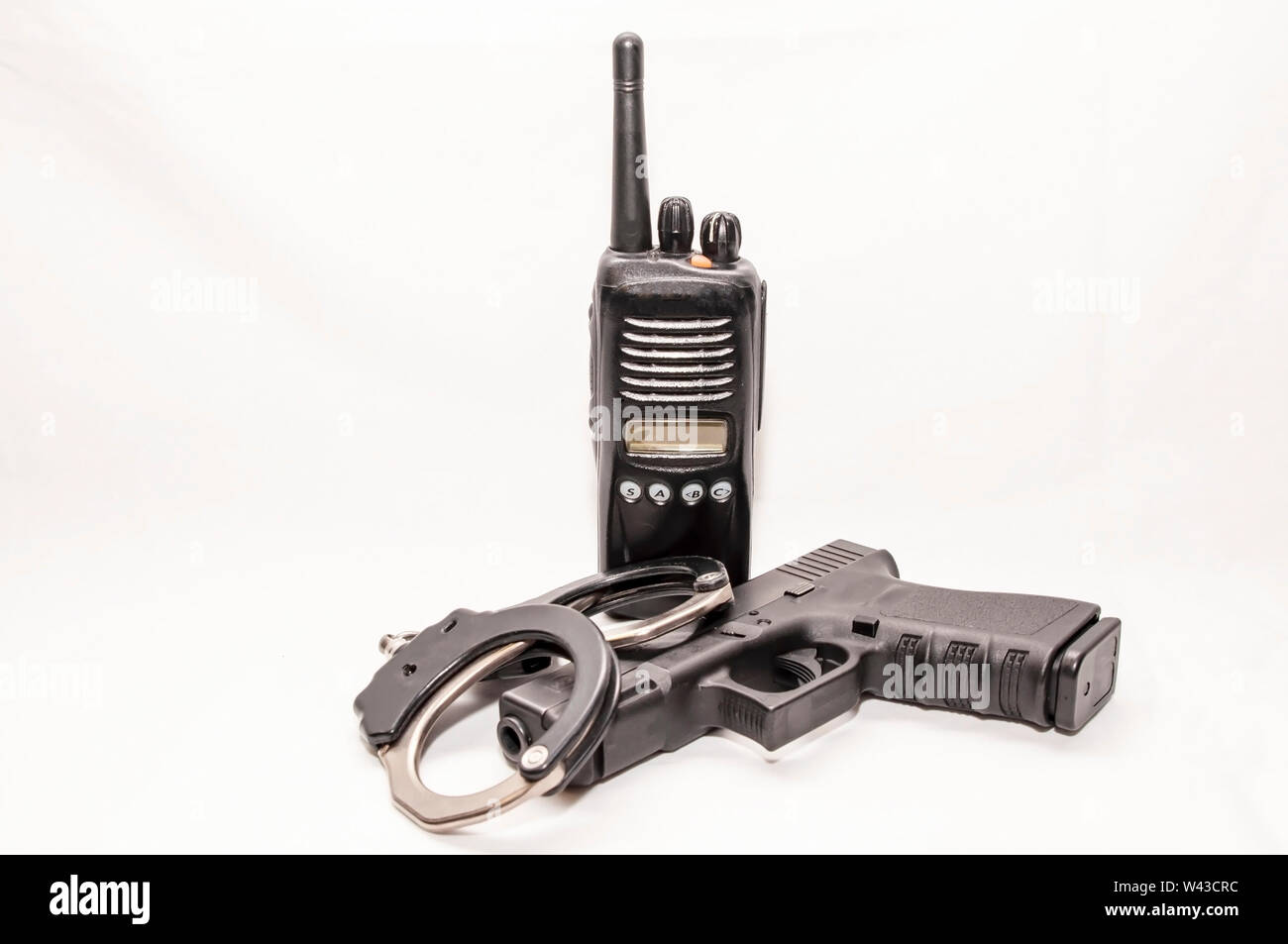 A set of black and silver handcuffs with a black 9mm pistol in front of a police radio with a white background Stock Photo