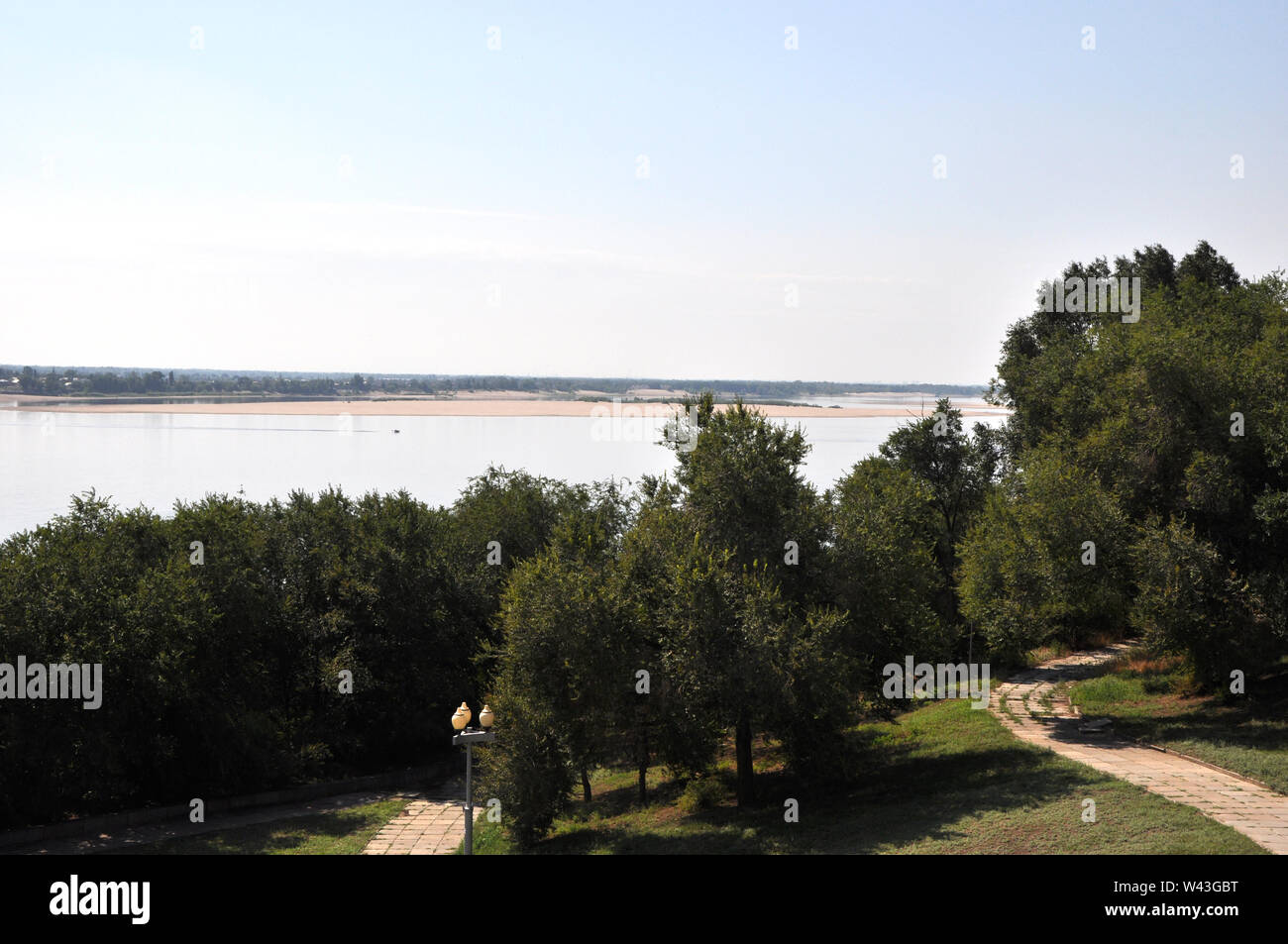 Green elm trees on a slope with paved alleys against summer morning riverscape Stock Photo