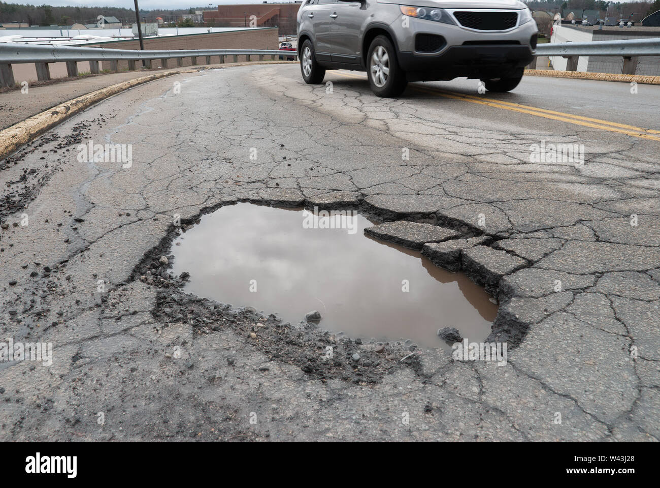 Water filled pothole on asphalted road with car avoiding the danger Stock Photo