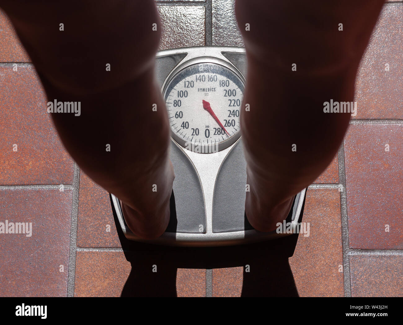 View of an overweight persons feet weighting themselves on a bathroom scale. Stock Photo
