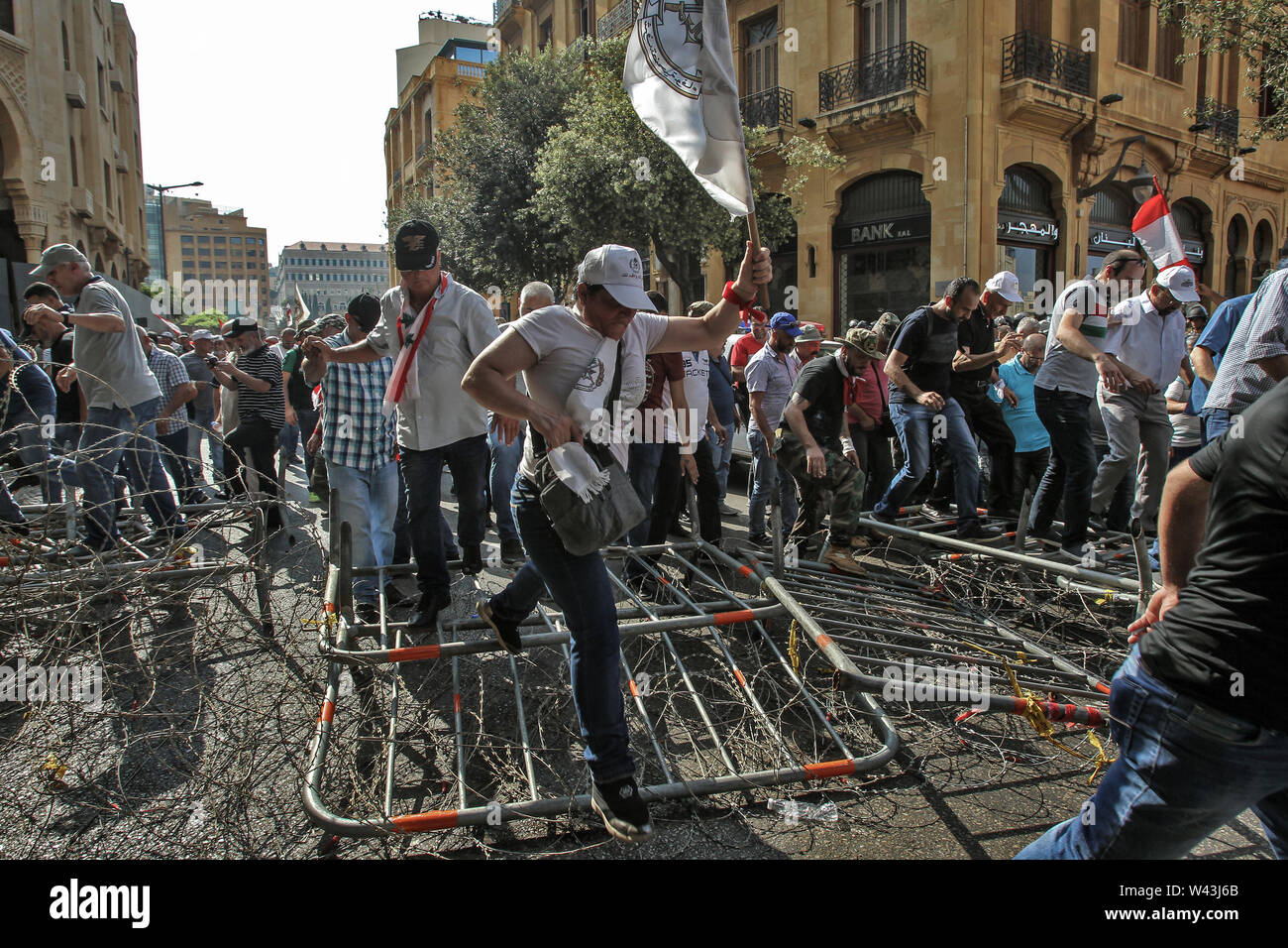 Beirut, Lebanon. 19th July, 2019. Lebanese retired soldiers and civilians  cross over barbed wire and barriers amid attempts to enter the Lebanese  parliament building where lawmakers and ministers approved the draft for