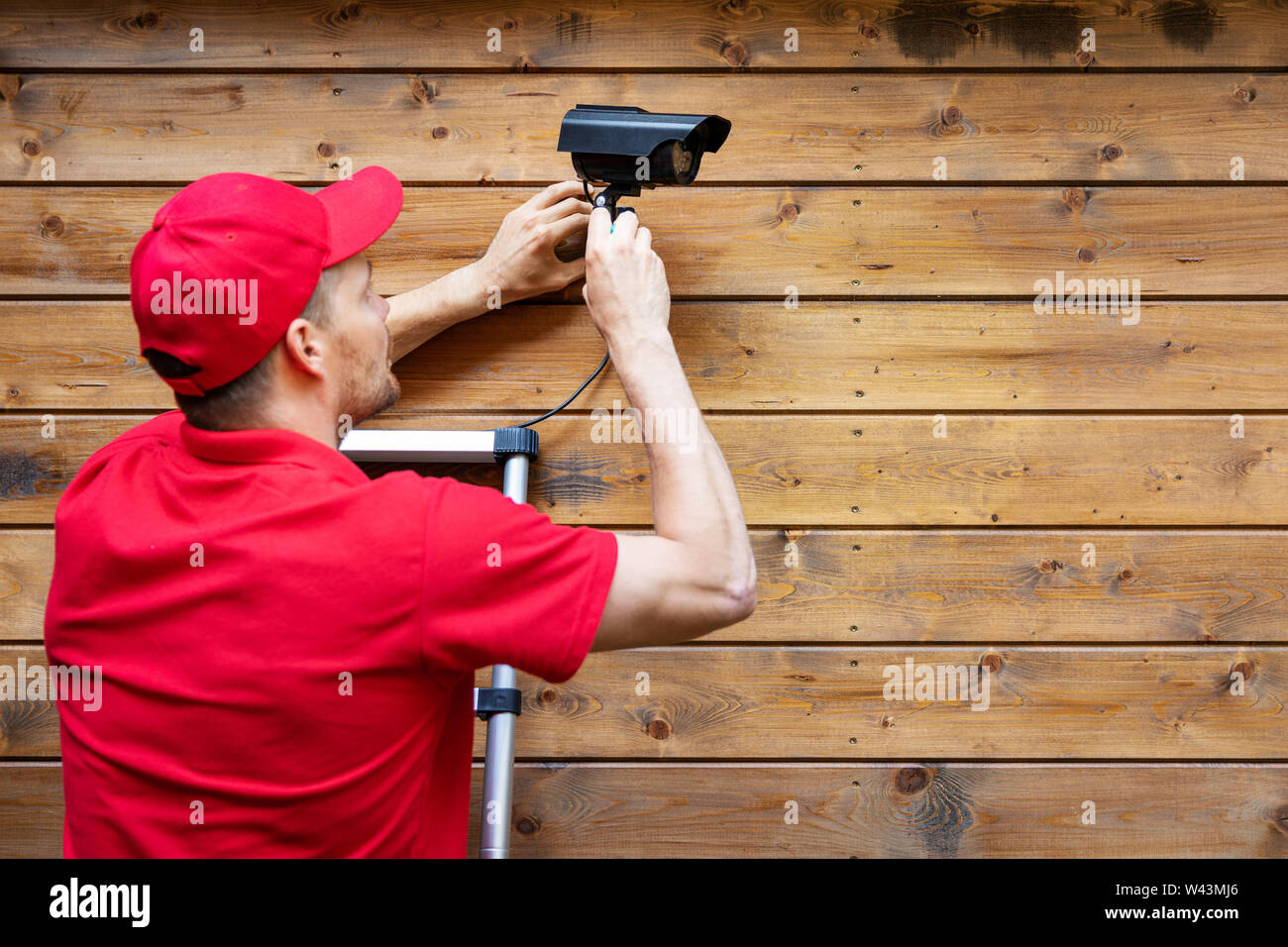 home security - man installing outdoor surveillance camera on wooden wall copy space Stock Photo