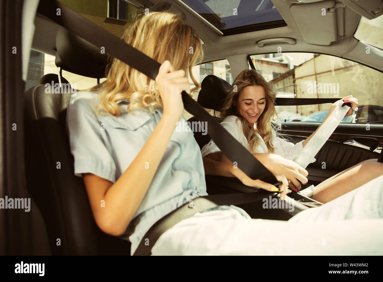 Young lesbian's couple preparing for vacation trip on the car in sunny day. Women sitting and ready for going to sea, riverside or ocean. Concept of relationship, love, summer, weekend, honeymoon. Stock Photo
