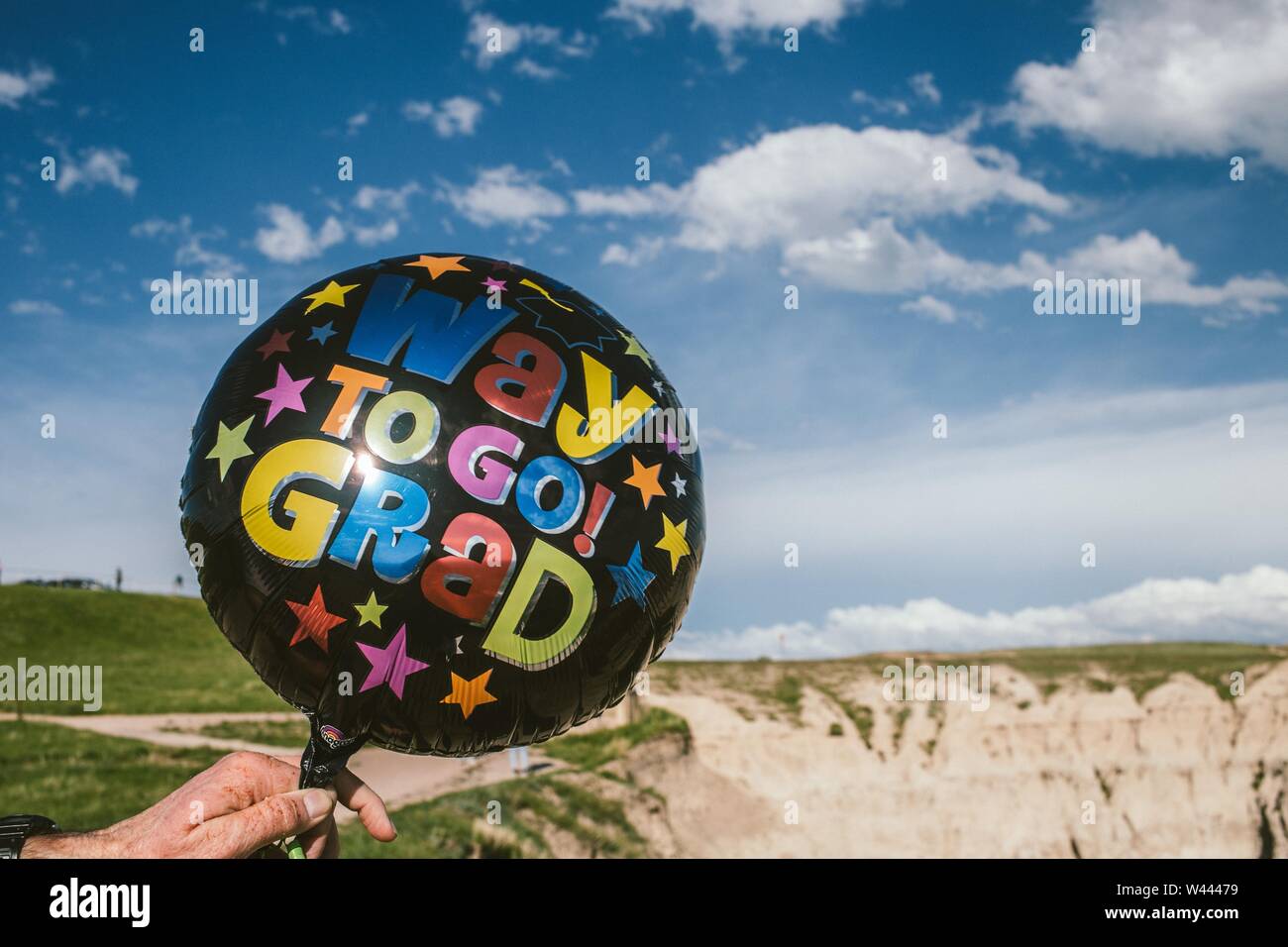 Closeup of a black balloon with a writing 'Way to go Grad' held by a person in the desert Stock Photo