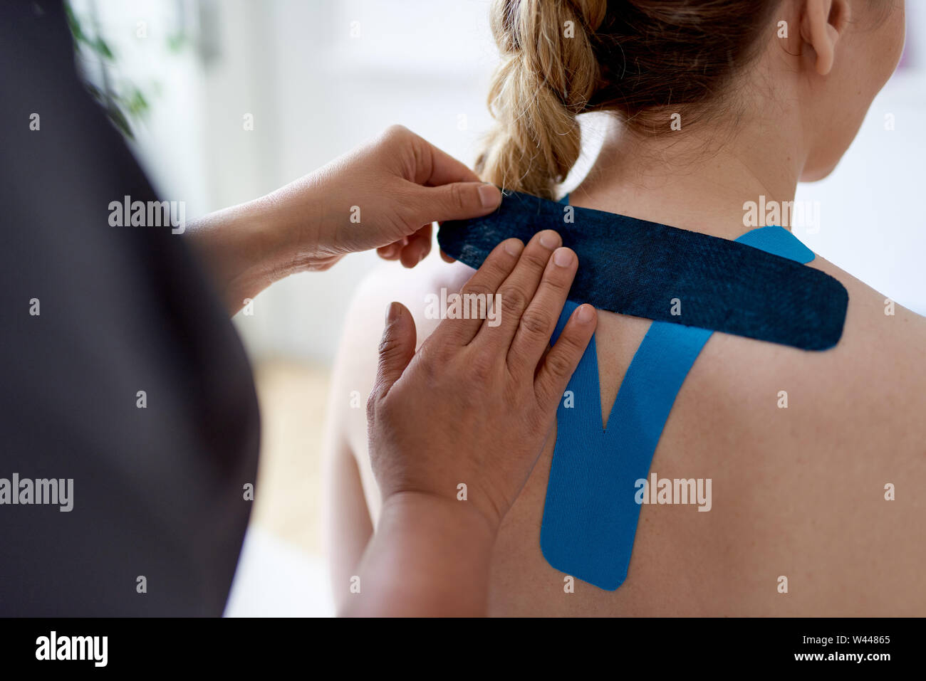 Chinese woman massage therapist applying kinesio tape to the shoulders and neck of an attractive