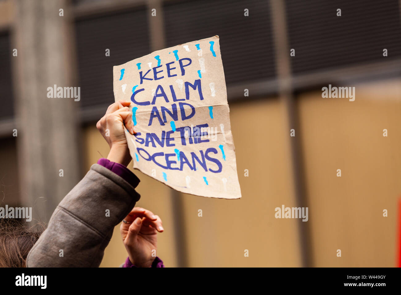 An ecological activist holds a homemade placard saying keep calm and save the oceans on an urban street during a climate change protest. Stock Photo