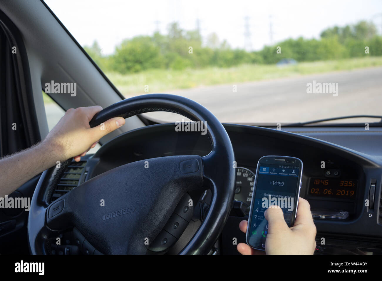Distraction behind the wheel concept. A man dials a phone number on touch screen of smartphone while driving a car. View from behind. Safe journey. Ph Stock Photo