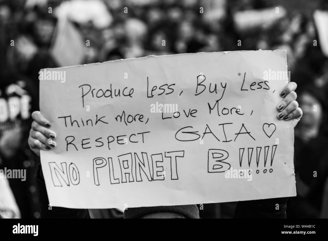 A closeup and monochrome view of a poster saying produce less, buy less, think more, love more, respect Gaia, no planet b, held by an ecological activist Stock Photo