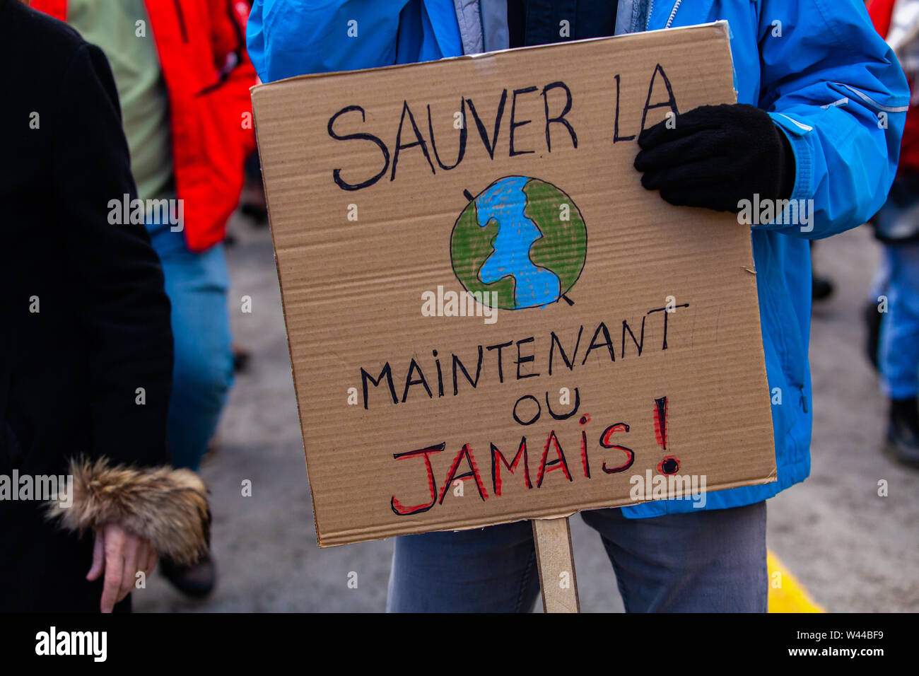 A French sign reads save it now or never and depict earth, held