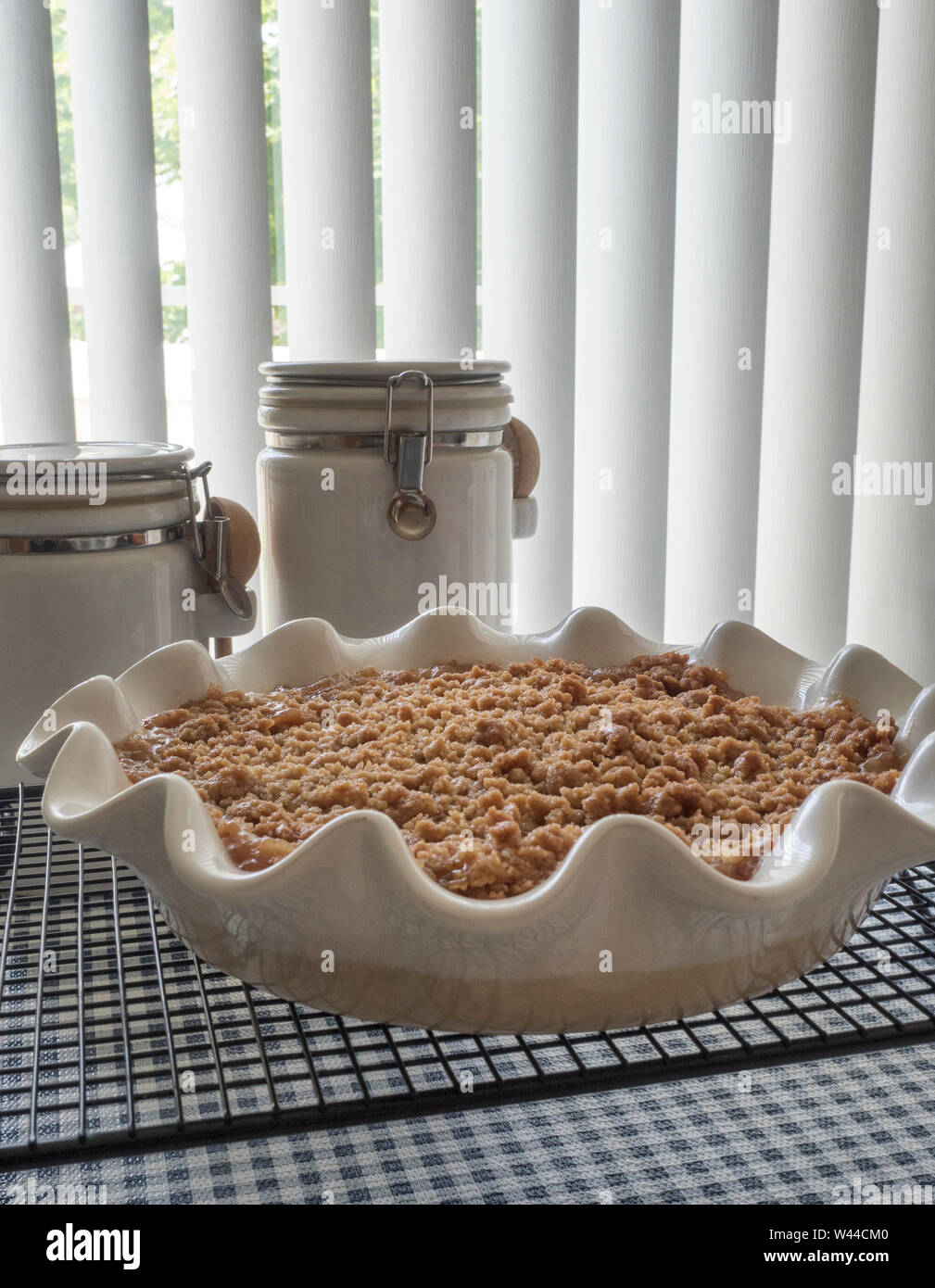 A whole streusel topped pie sits on a baking rack, with baking ingredient containers in the