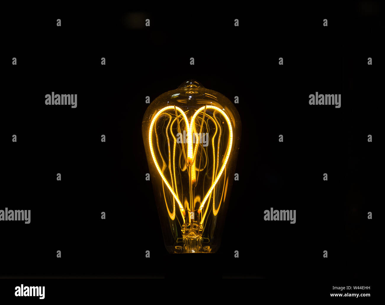 Lightbulb on dark background with bright wire in shape of a heart Stock