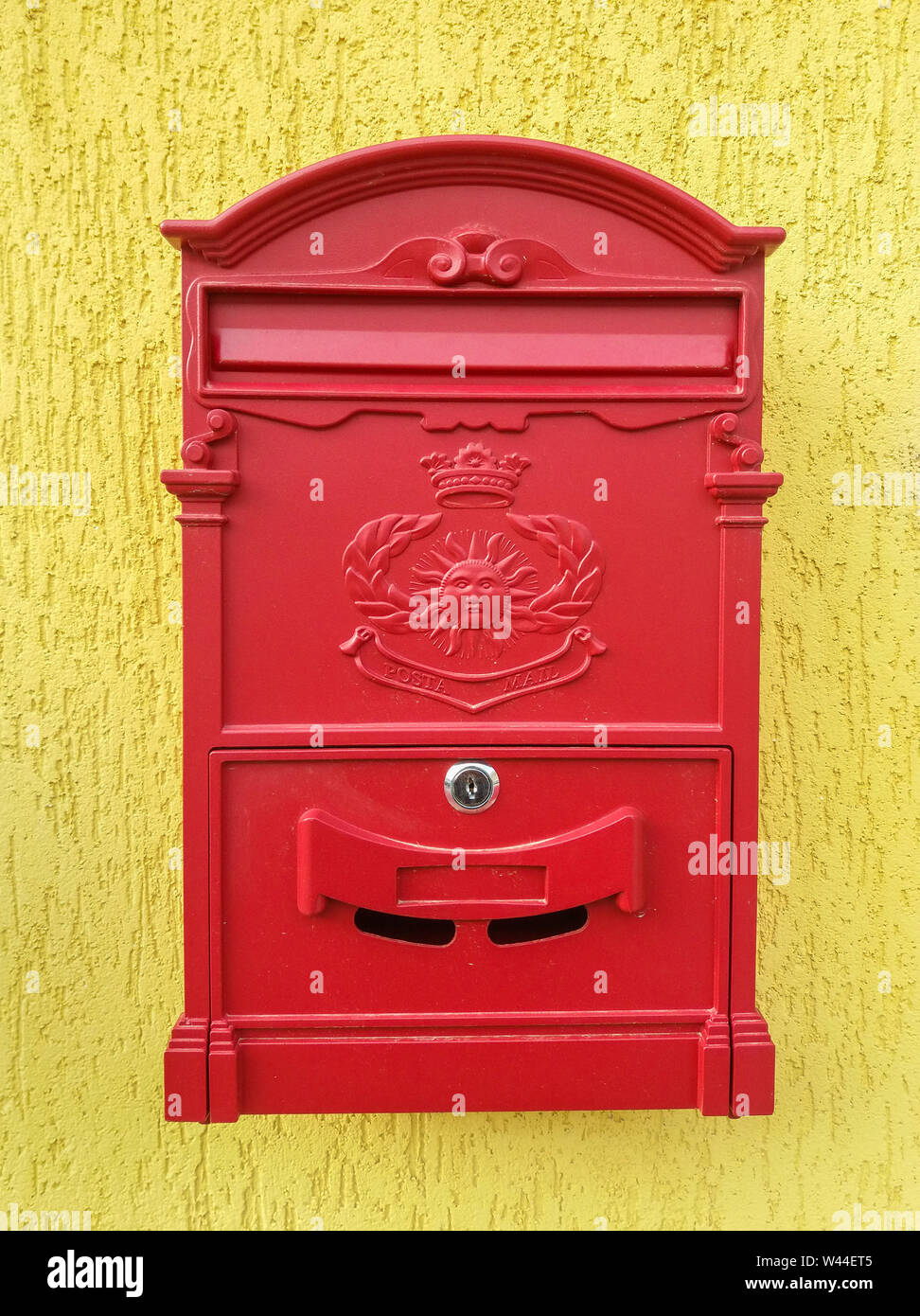 Red metal mailbox on a yellow wall Stock Photo