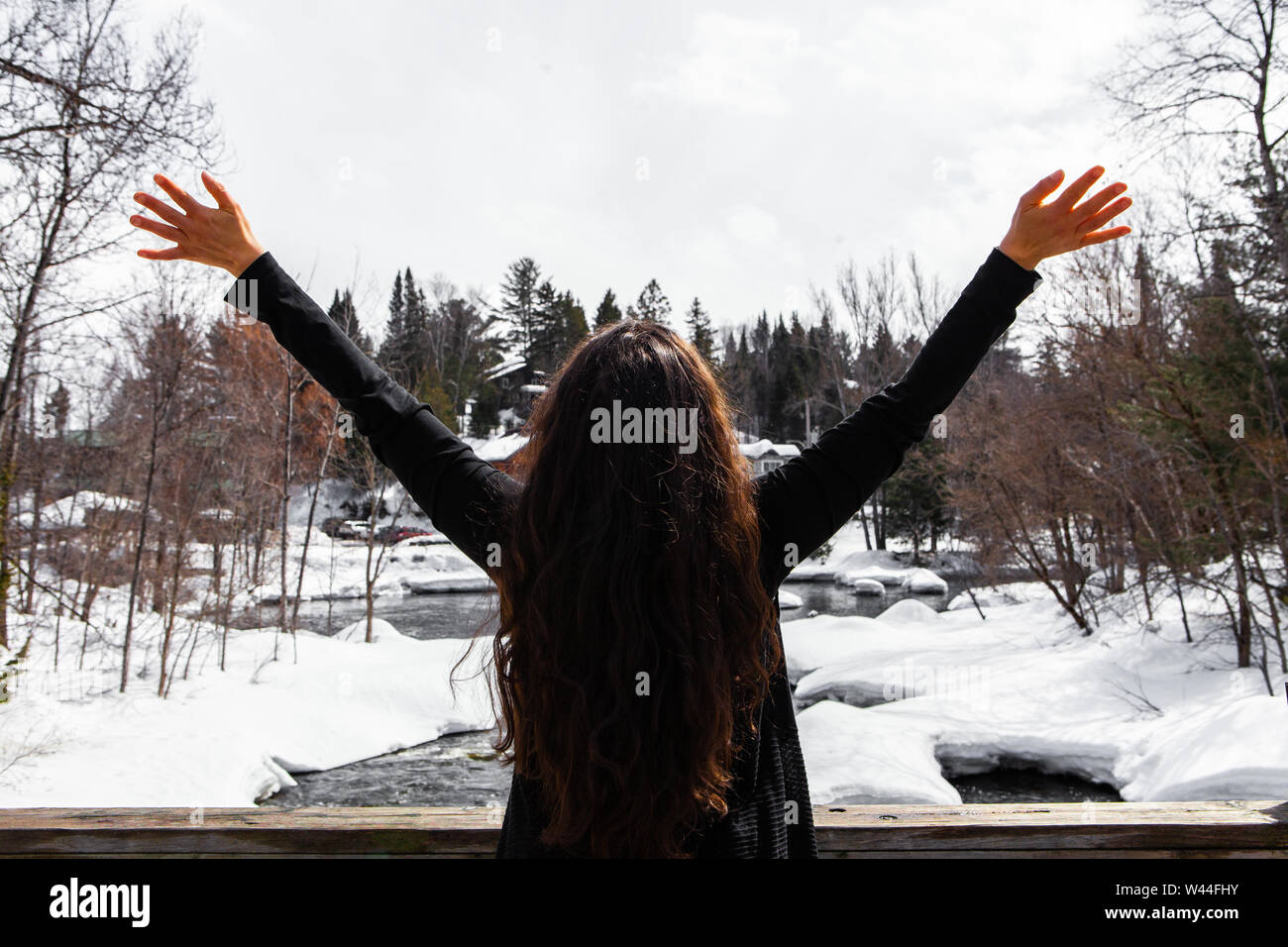 A young female is viewed from the back, gives an excited expression at the beautiful snowy landscape in the background, enjoys winter surroundings Stock Photo