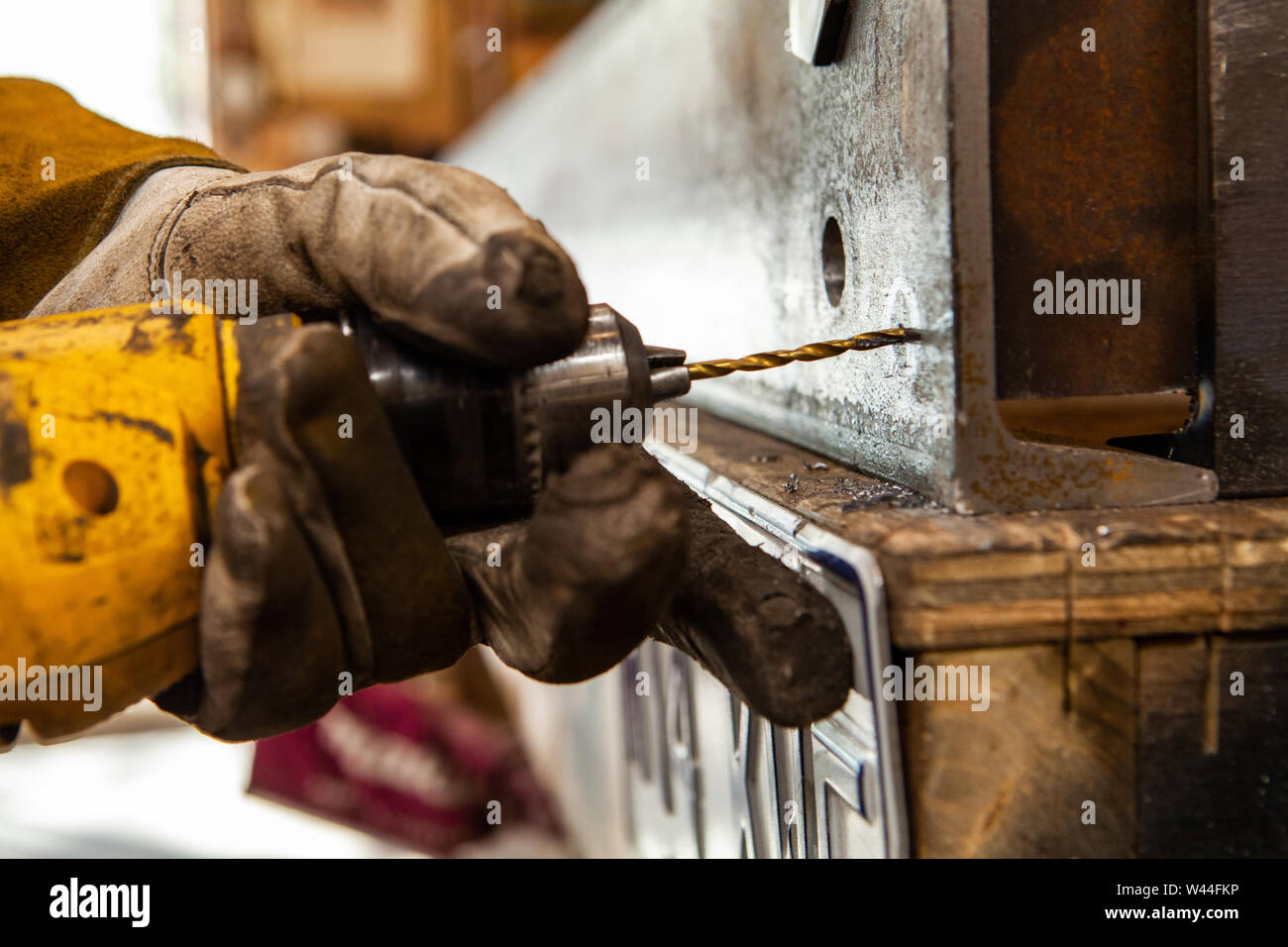 A close up shot of a blacksmith wearing protective gloves whilst drilling a hole through a thick piece of metal. Spotting drill bit used for marking steel. Stock Photo