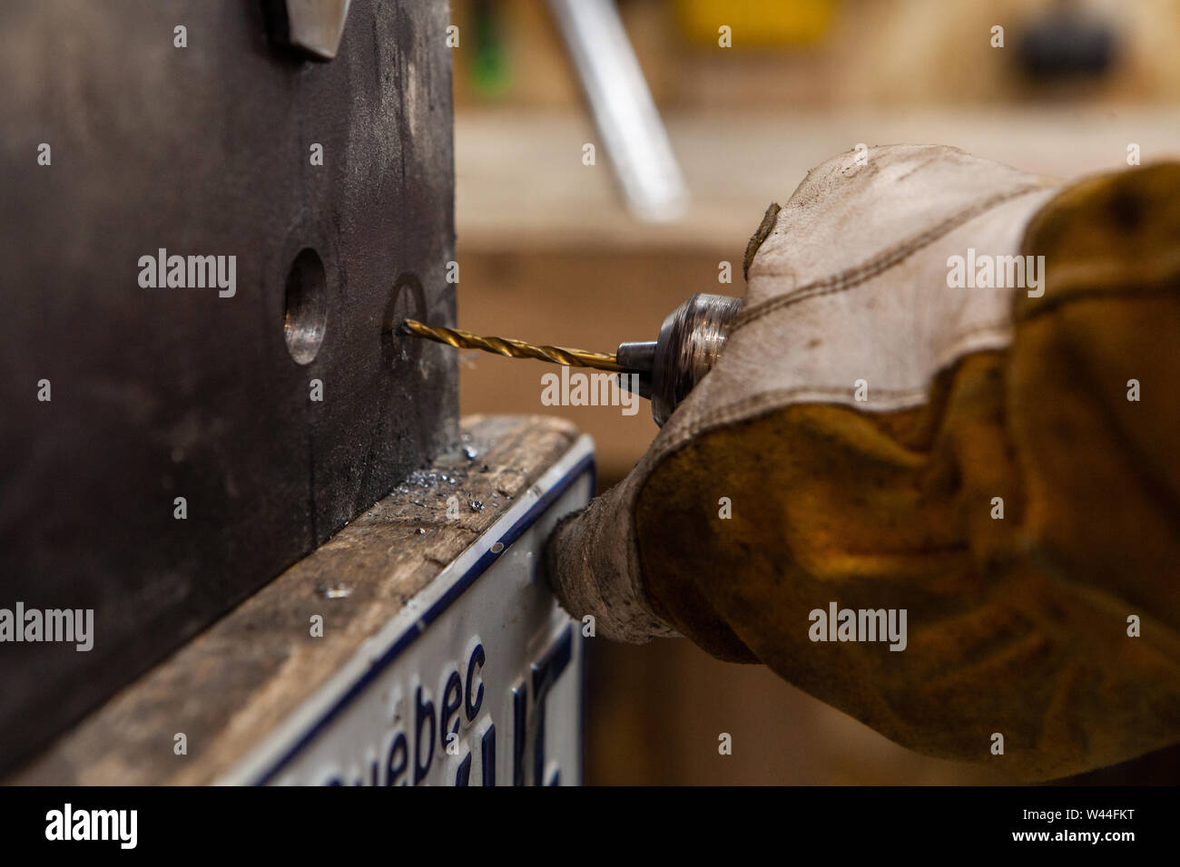 A closeup view on a metalworker using a power drill to put a pilot hole through a heavy duty steel beam. Worker wearing protective gloves drilling hole. Stock Photo