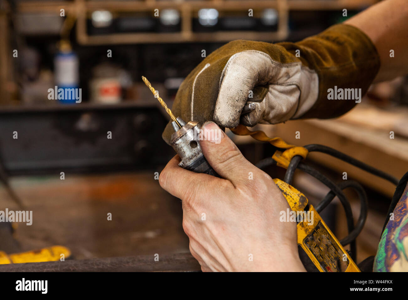 A closeup view on the dirty hands of a metalworker using the chuck of a power drill to replace a spotting bit, used for marking and drilling holes in steel. Stock Photo