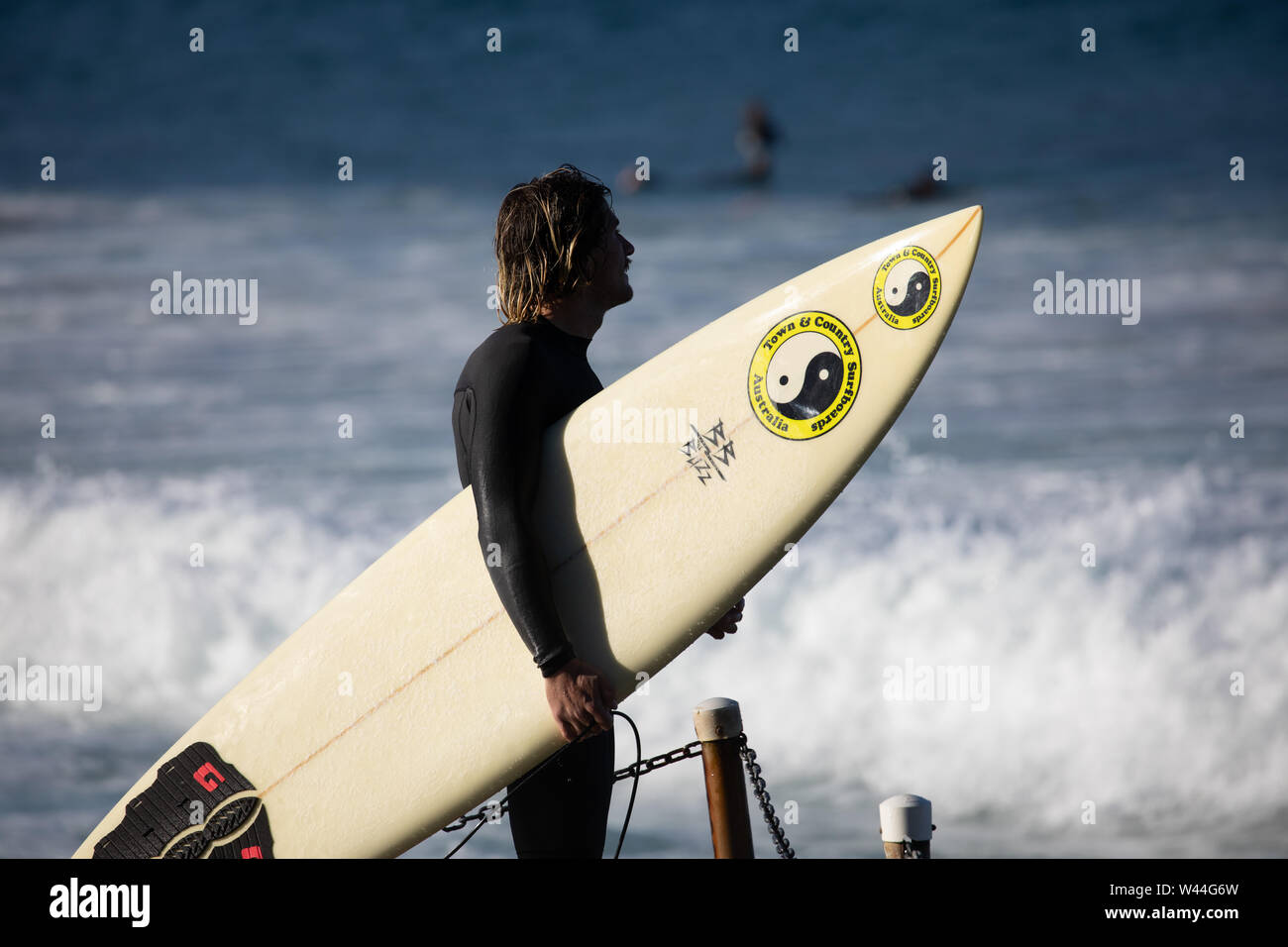 Man in wetsuit carries surfboard to the ocean surf at a Sydney beach in