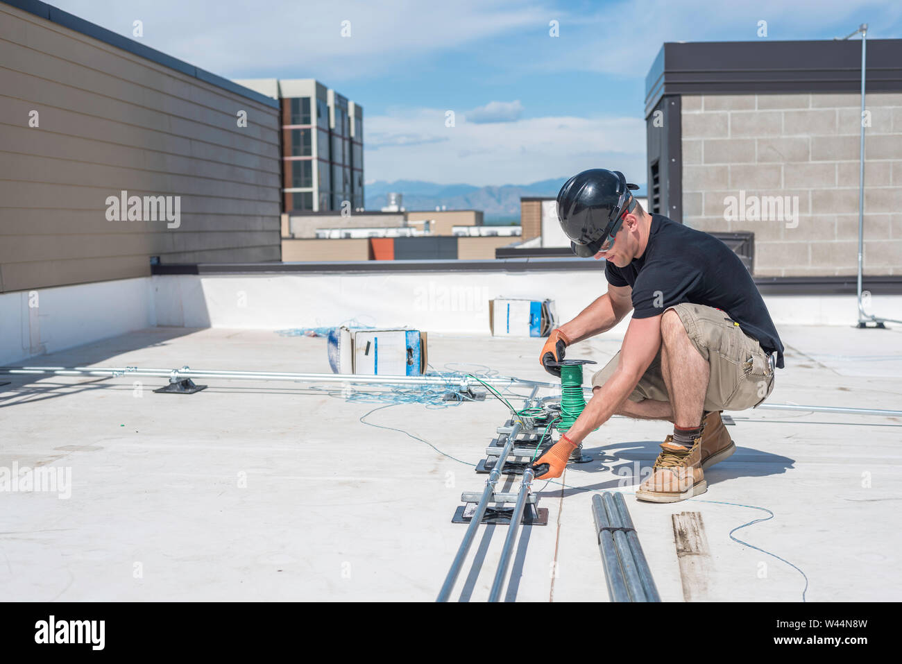 Electrician running wire through conduit on a building roof top Stock