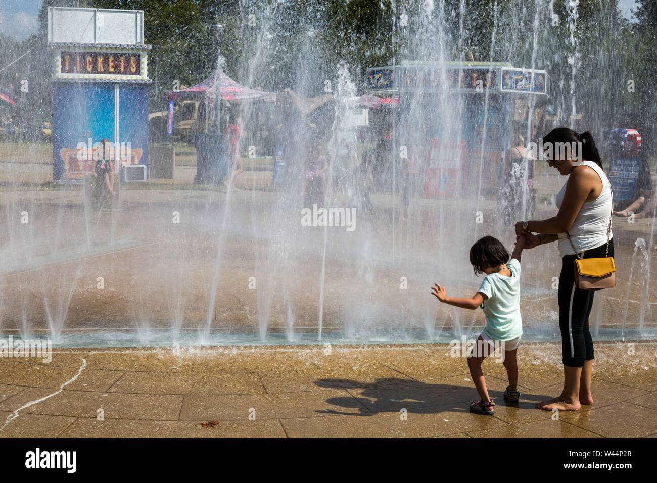 A mother encourages her timid daughter to enjoy the splash pad at the Three Rivers Festival in downtown Fort Wayne, Indiana, USA. Stock Photo