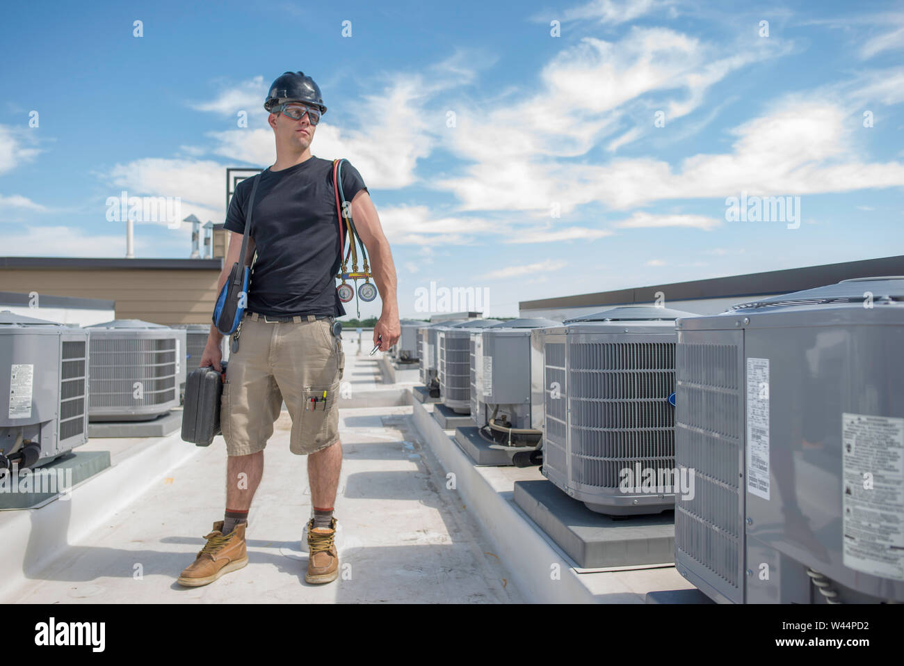 Hvac technician standing in between 2 rows of condensers, holding