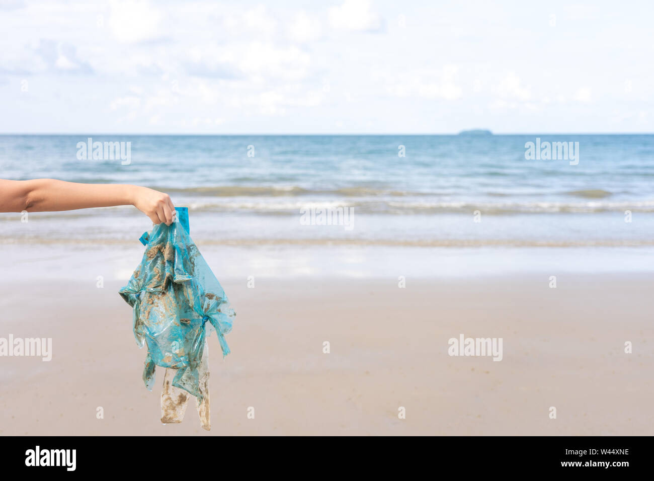 Woman’s hand picking up used plastic bag on sand beach, cleaning