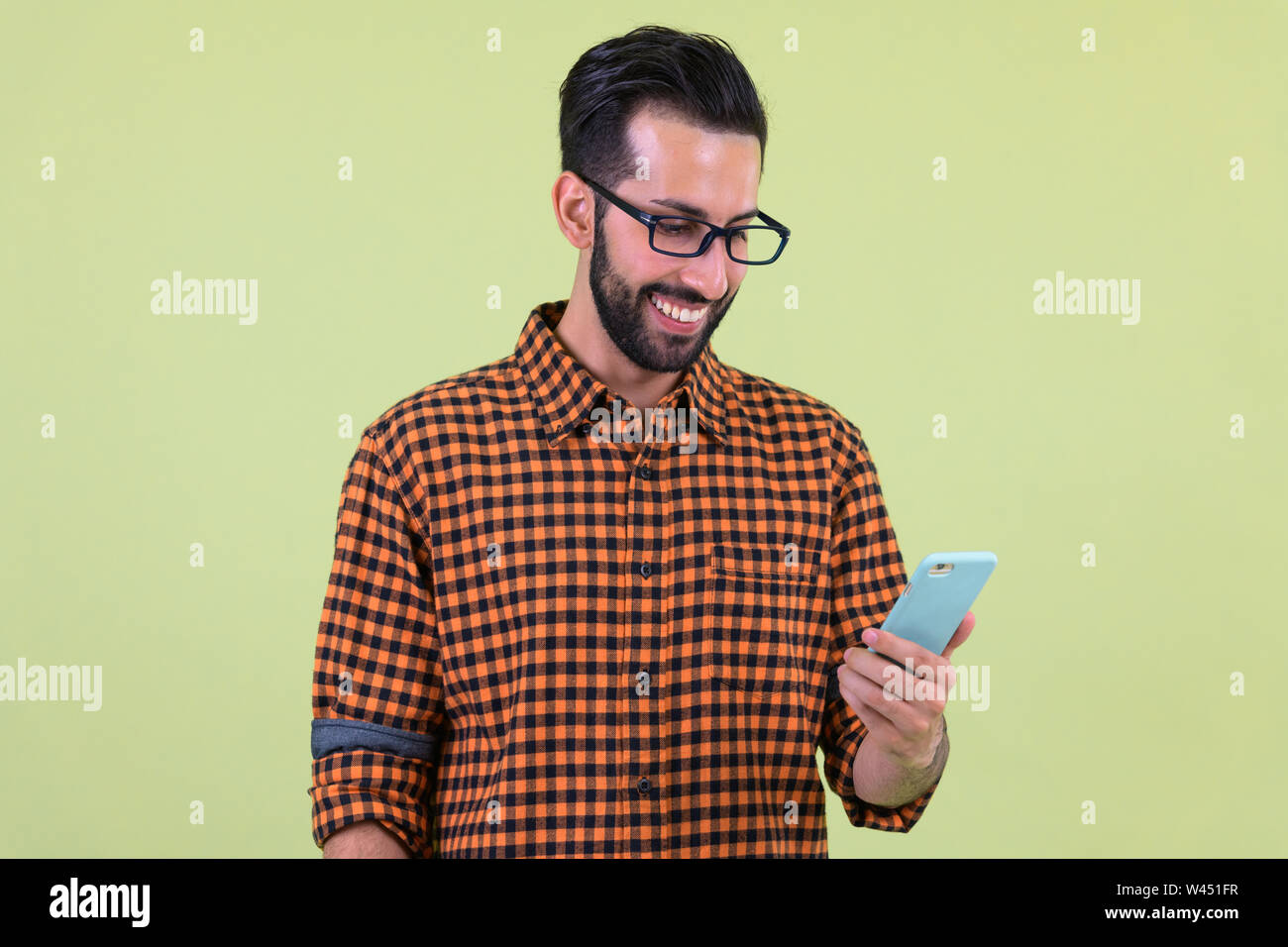 Happy young bearded Persian hipster man using phone Stock Photo