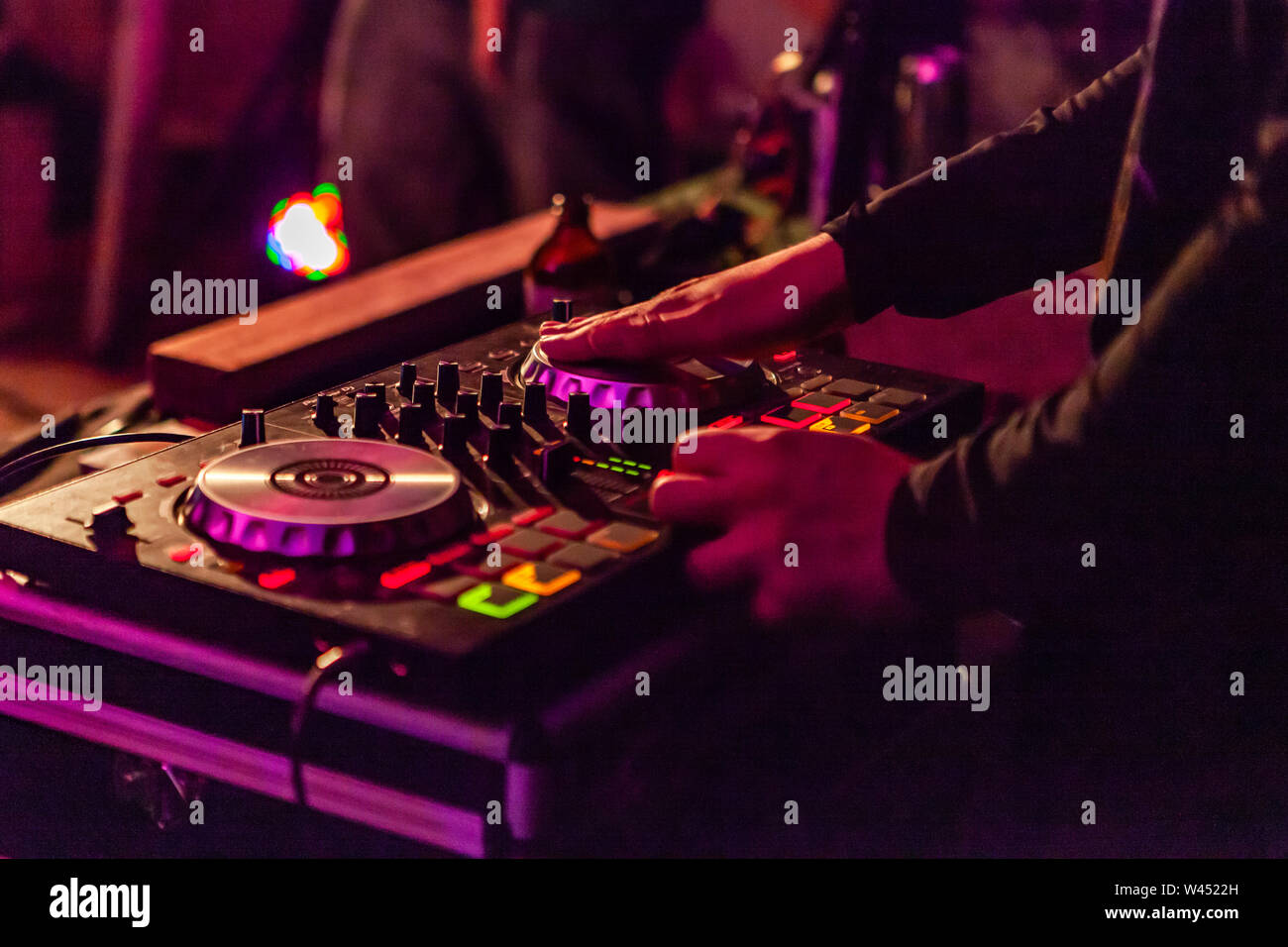 Hands of a DJ are viewed close up performing turntablism on modern mixing equipment, pictured outdoors by night under artificial lighting. Stock Photo
