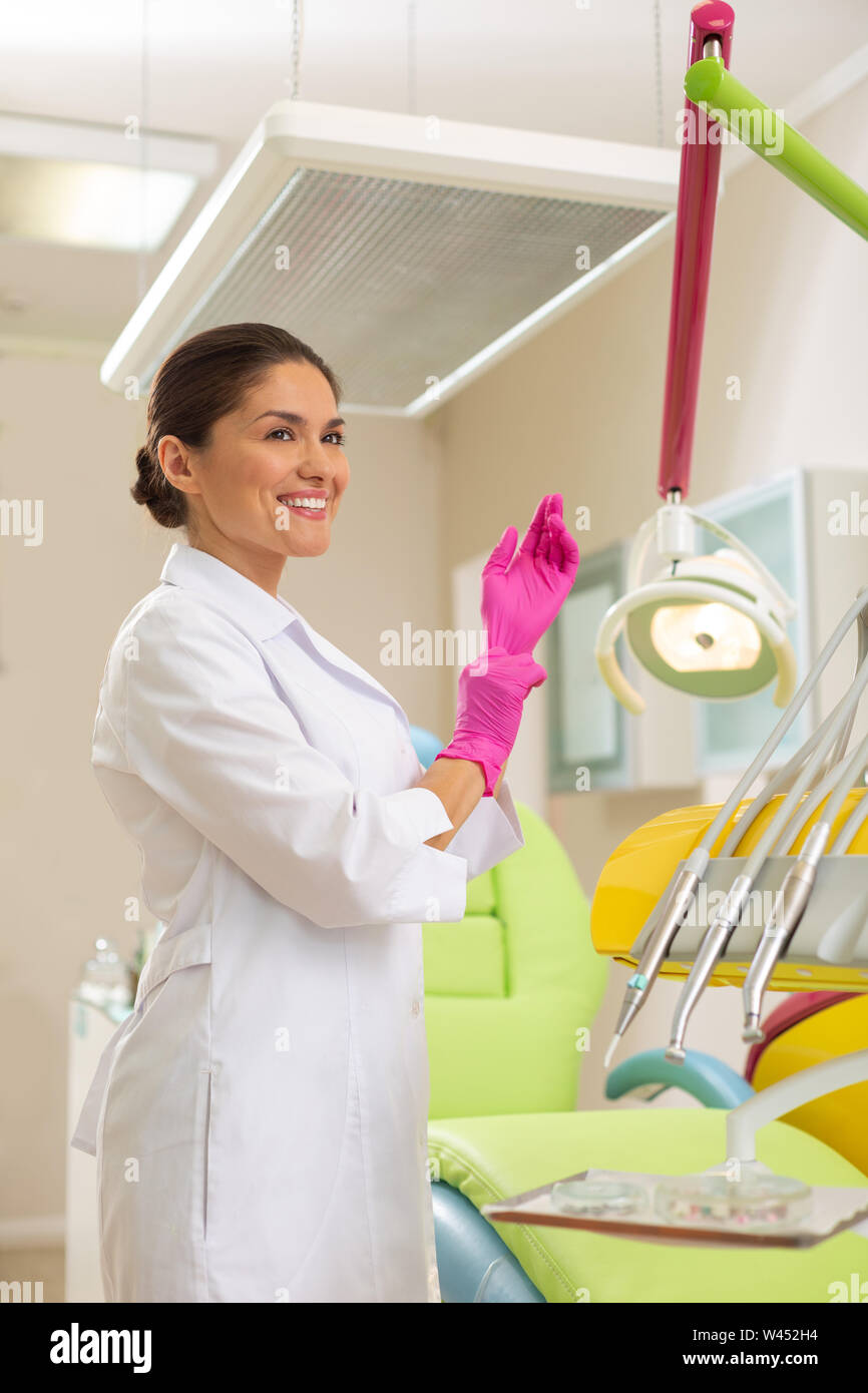 Smiling middleaged female dentist putting on aseptic gloves Stock