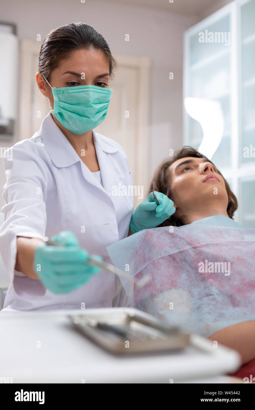 Serious middleaged female doctor taking a dental mirror Stock Photo