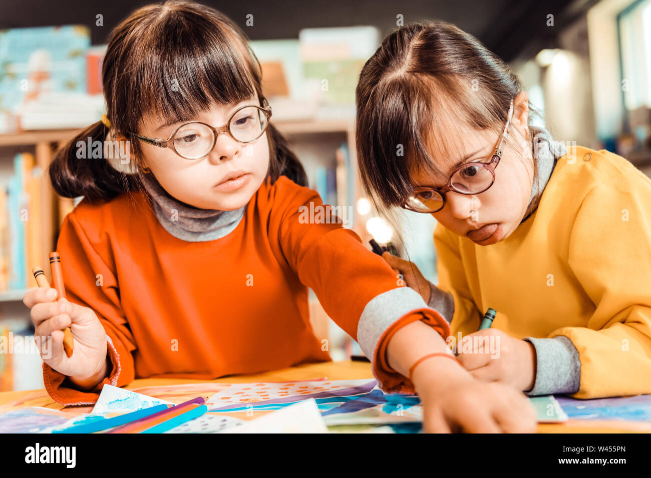 Curious dark-haired girl in eyeglasses taking new color of pencil Stock Photo