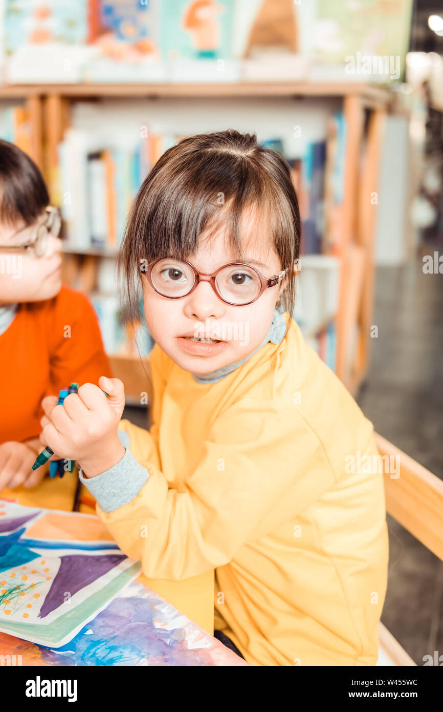 Dark-haired young girl with long bangs and eyeglasses wearing yellow sweater Stock Photo