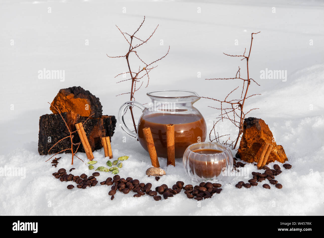 Natural ingredients are seen close-up, by a glass jug of freshly blended chaga chai latte, warm drink prepared in the snow, believed to have magical properties Stock Photo