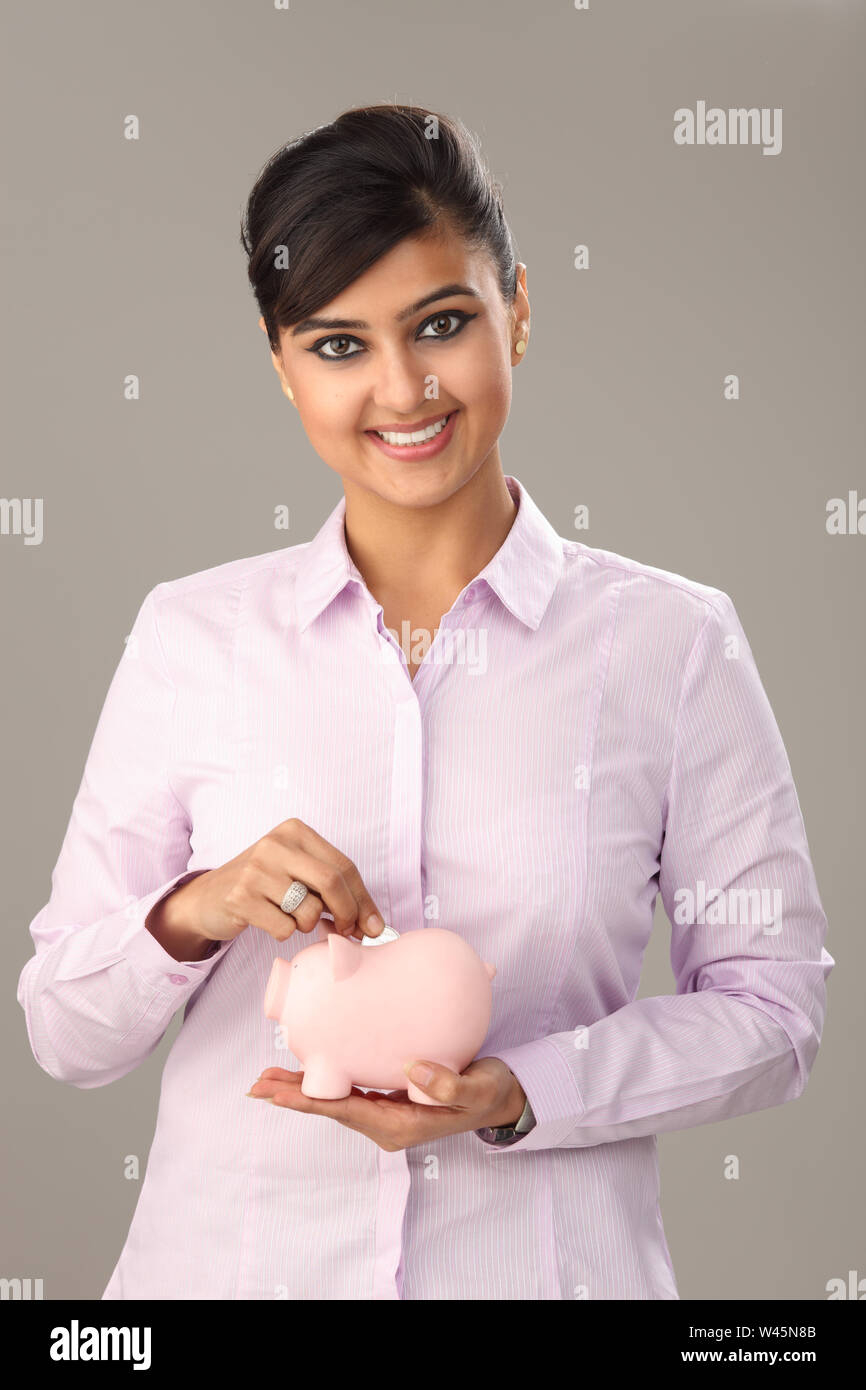 Businesswoman inserting coin into a piggy bank and smiling Stock Photo ...