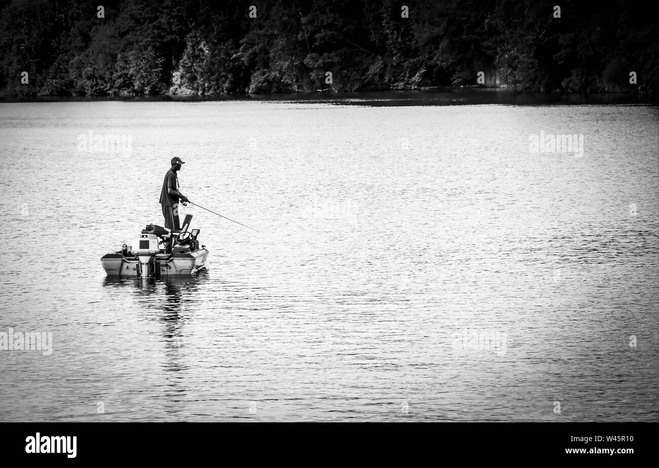 An Africian America man fishing from his powerboat, pratically in shillioute, in the middle of the river in the Southeastern USA, in black and white Stock Photo