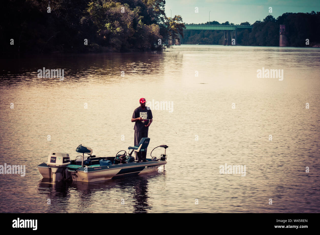 An African America man fishing from his motorboat, practically in silhouette, at sunset, on the river in the Southeastern USA Stock Photo