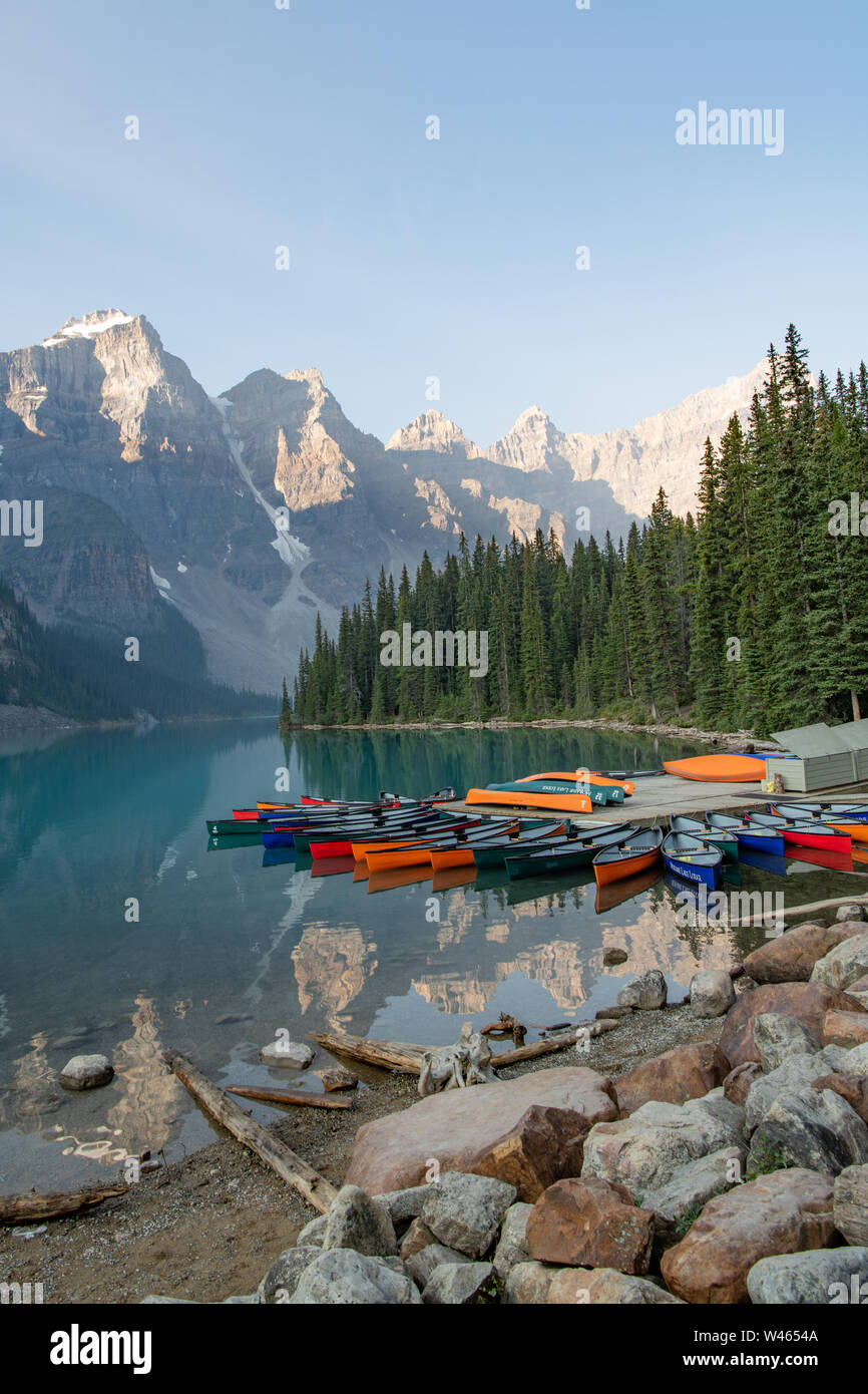 canoes piled up on the shores of Moraine lake with reflections in glacial lake of mountains behind near Banff Alberta, Canada Stock Photo