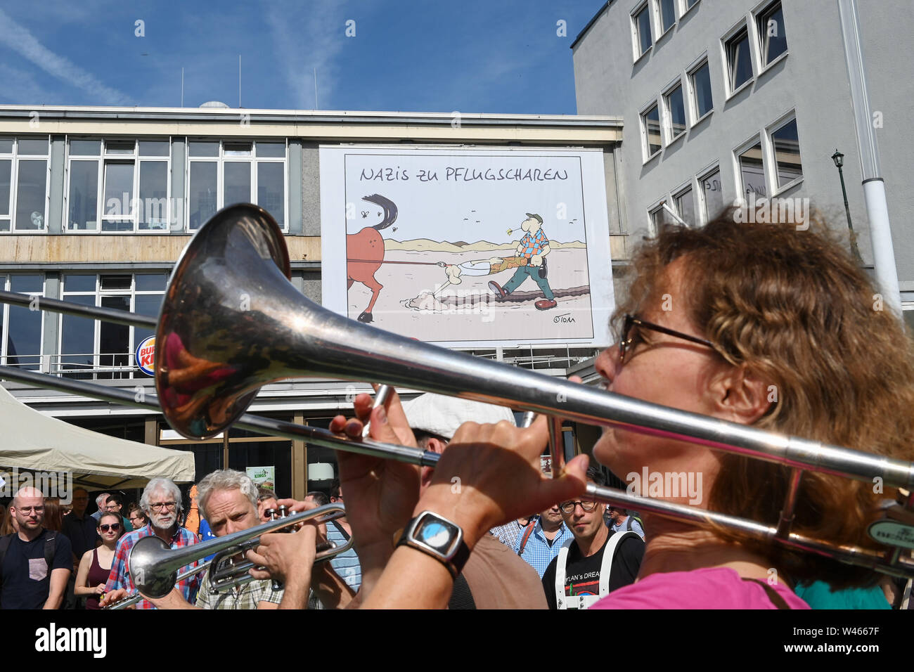 Kassel, Germany. 20th July, 2019. During a demonstration against the march of the small party 'Die Rechte' in front of a big cartoon in front of the Caricatura, a woman blows her trombone. The party had called for a demonstration in Kassel against media prejudgement in connection with the Lübcke case. A massive police presence is to prevent possible riots between the two camps. Credit: Uwe Zucchi/dpa/Alamy Live News Stock Photo