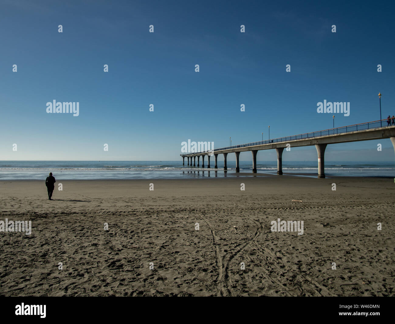 One person on beach by the pier in autumn with blue skies, New Brighton, New Zealand Stock Photo