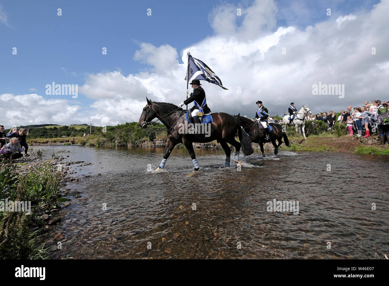 Kelso, Scotland, UK. 20th July 2019.    Kelso Civic Week  - Yetholm Ride out, Kelso. Kelso Laddie Mark Henderson carries the Town Flag (Standard) as he fords the Bowmont Water ahead of the 200 strong mounted cavalcade with RHM Sean Hook (2018 KL), Craig Logan (2017 KL), on the ride out to Yetholm Saturday 20 July 2019.   (Credit: Rob Gray ) Credit: Rob Gray/Alamy Live News Stock Photo
