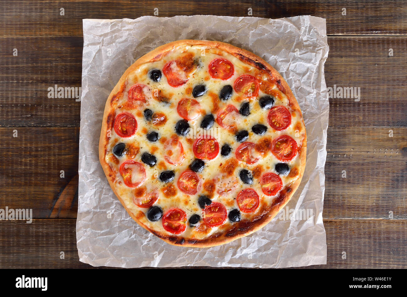 Appetizing homemade pizza with tomato and olives on paper over on wooden background, top view, flat lay Stock Photo