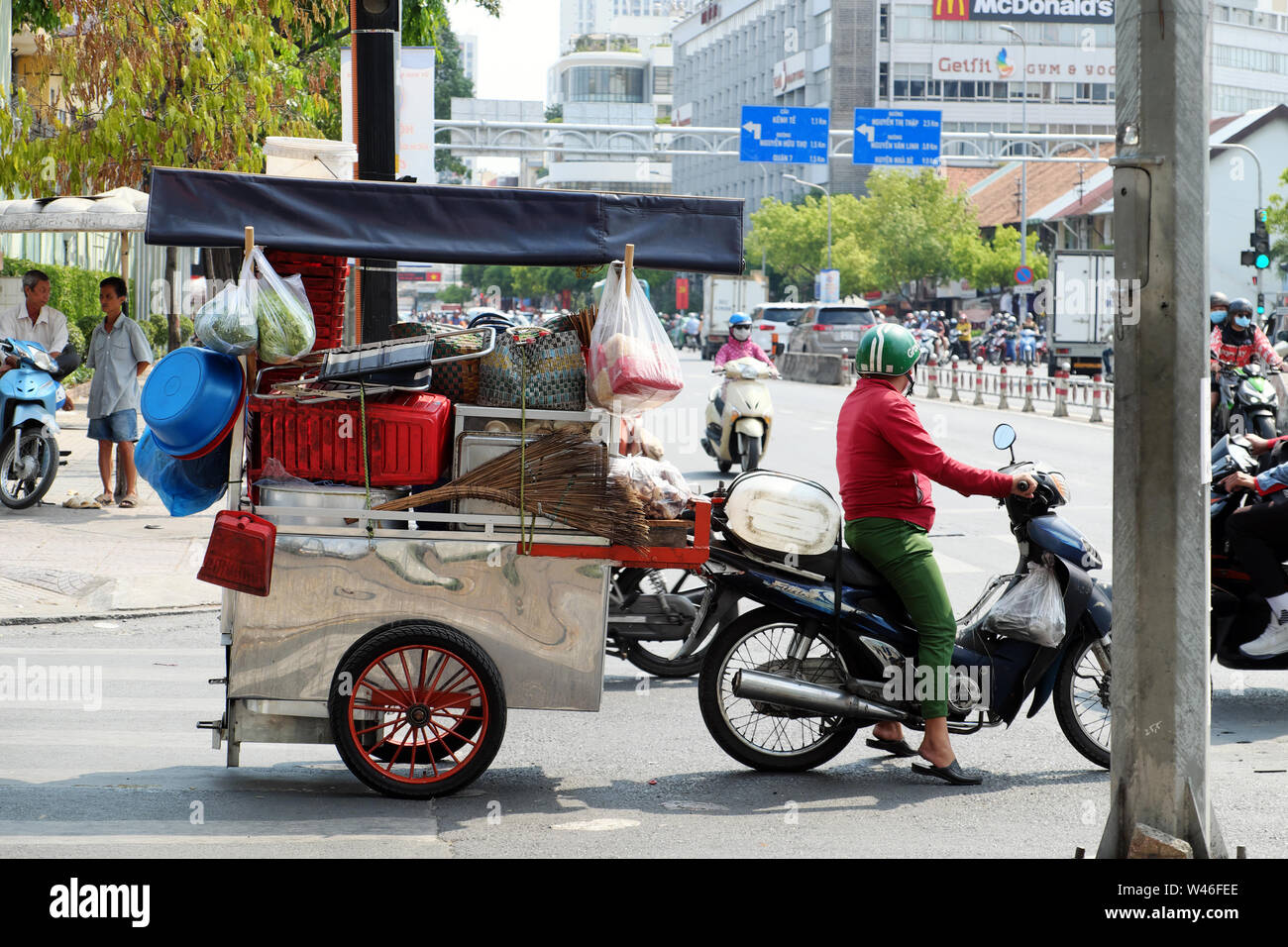 Vietnamese woman ride motorbike pull food cart stop on urban street on